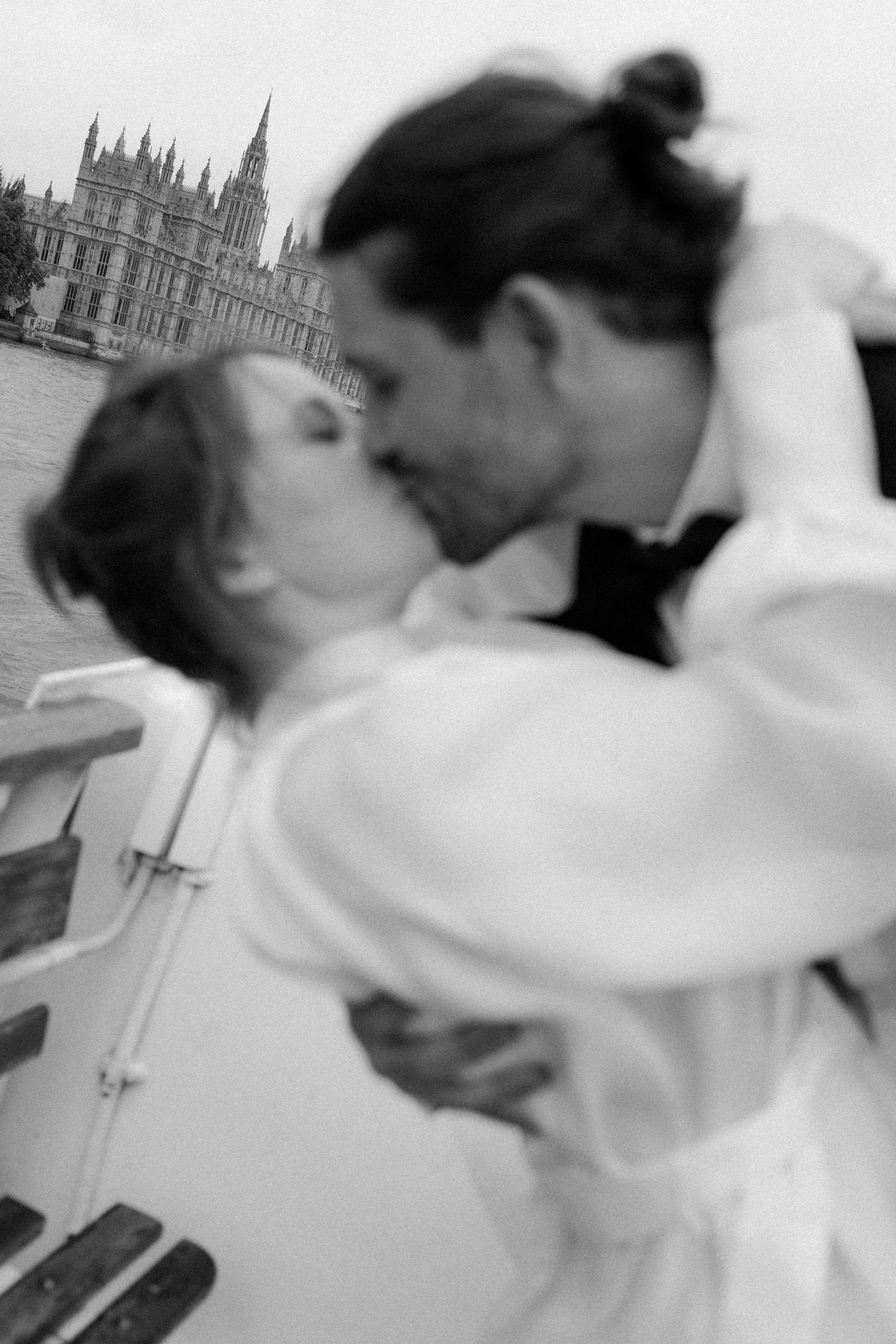 Black and white photo of a couple kissing on a boat with the Houses of Parliament in the background.