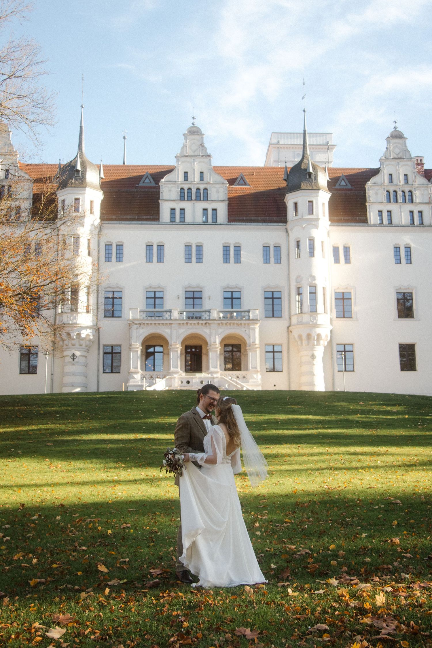 A couple dances on a green lawn in front of a grand white castle-like building with ornate architecture.
