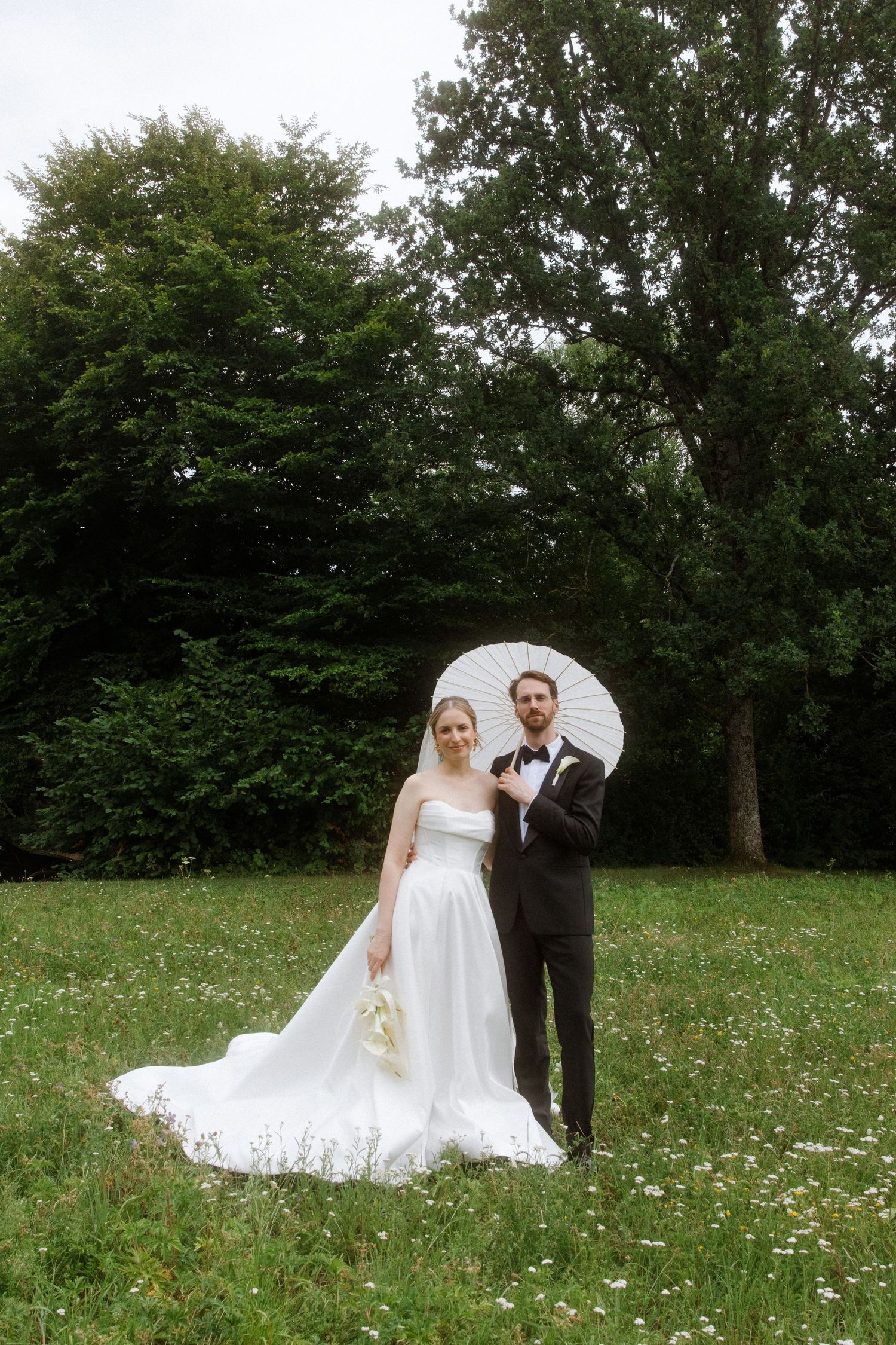 A wedding couple poses with a parasol in a field of wildflowers.