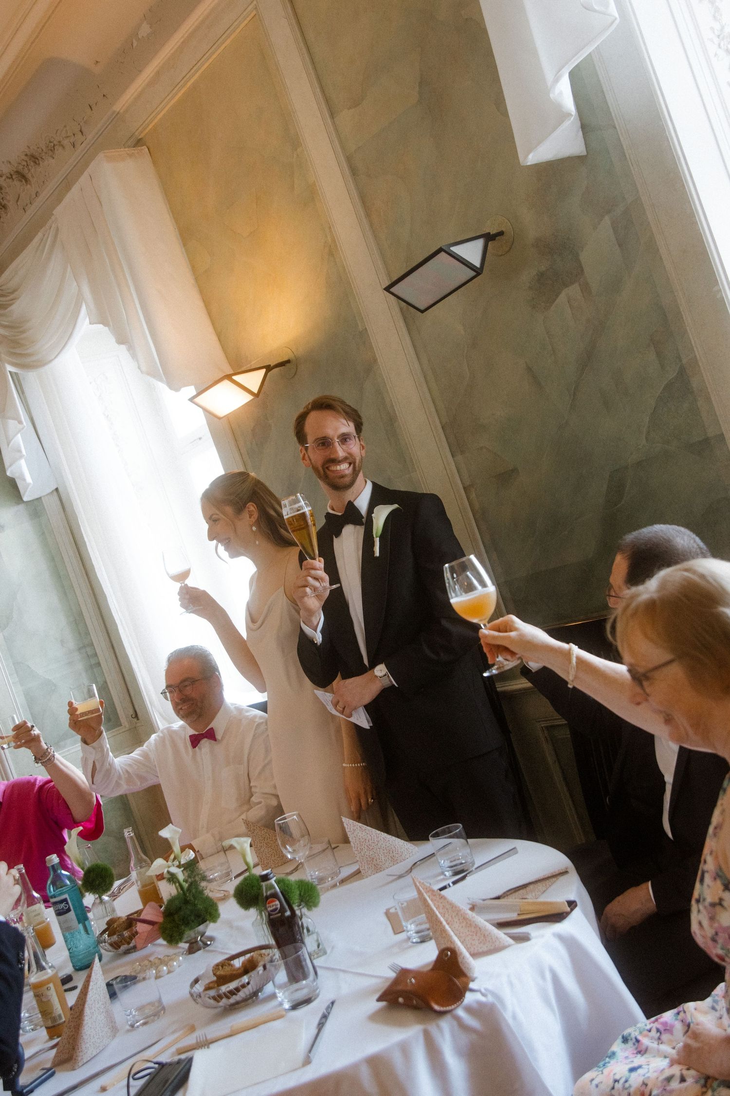 Wedding reception guests raising glasses for a toast in an elegant dining room.