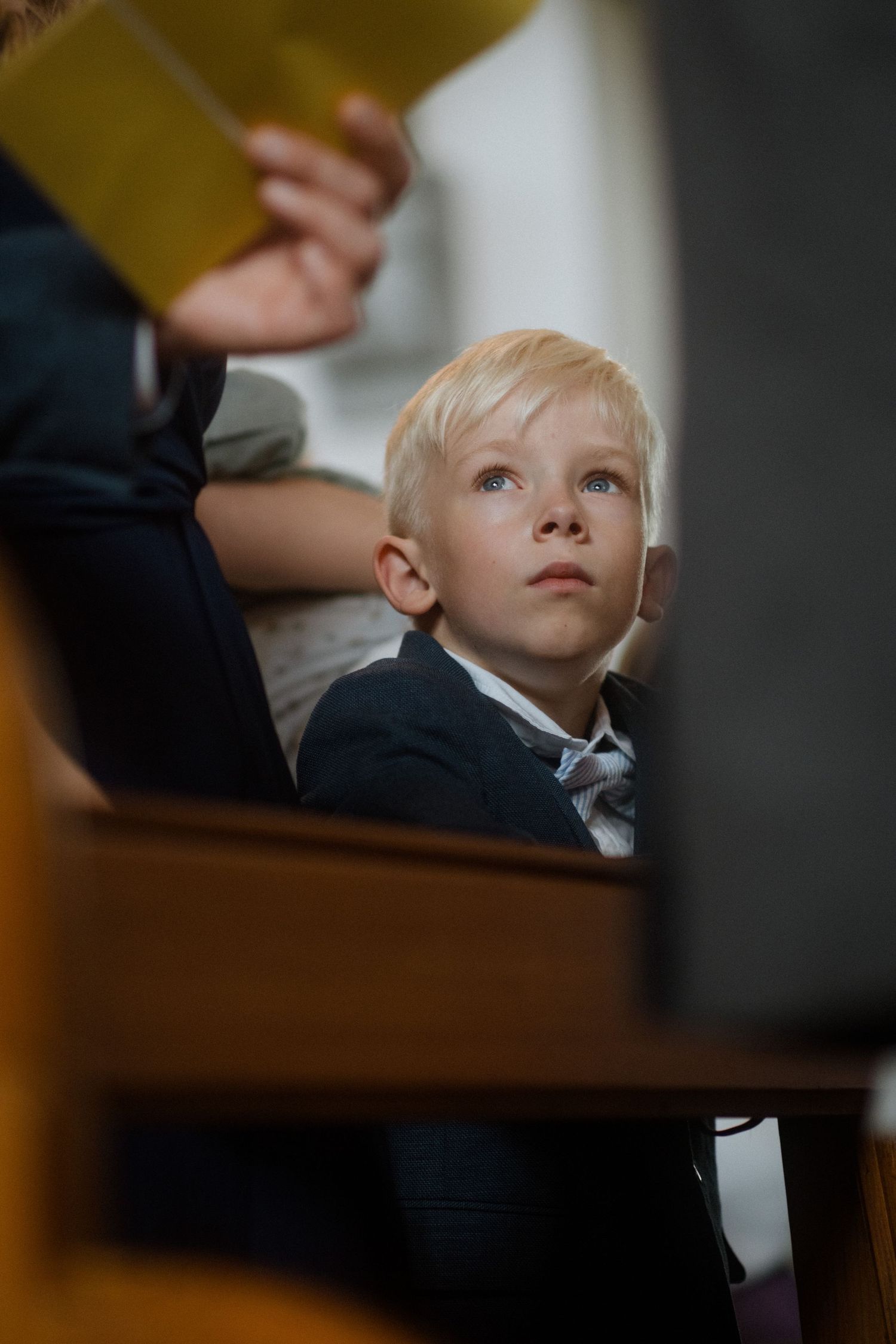 A young child in formal attire sits attentively in a church pew.