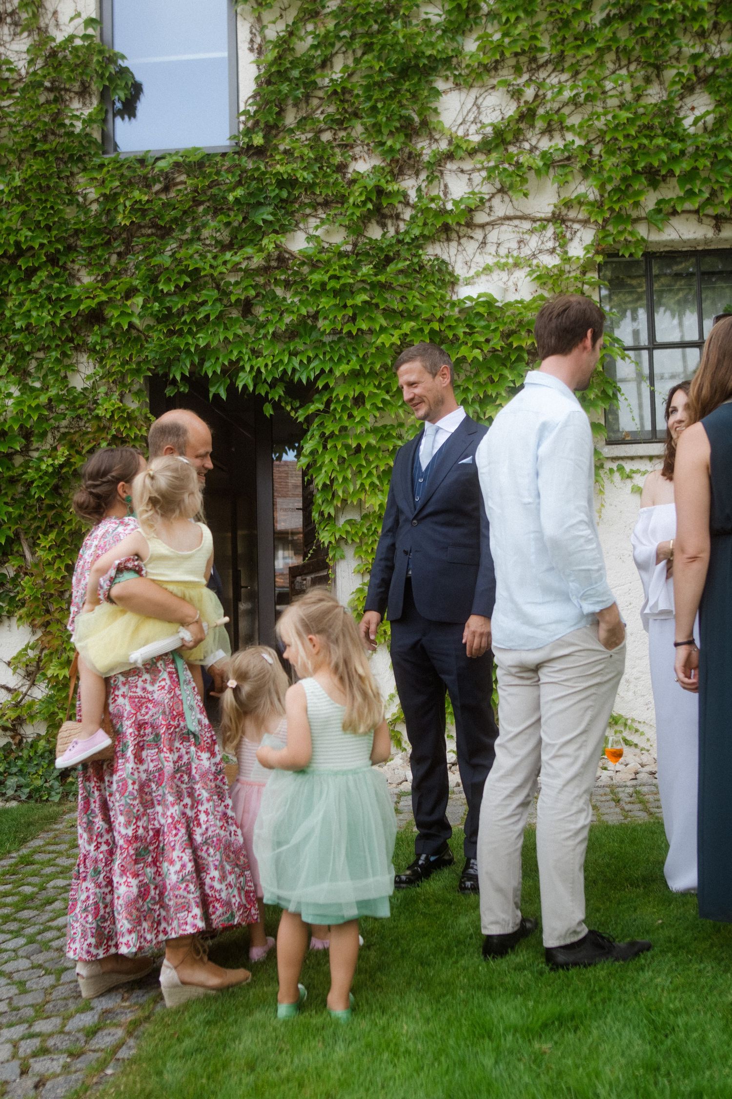 Guests and wedding party mingle outside a historic building with climbing vines.