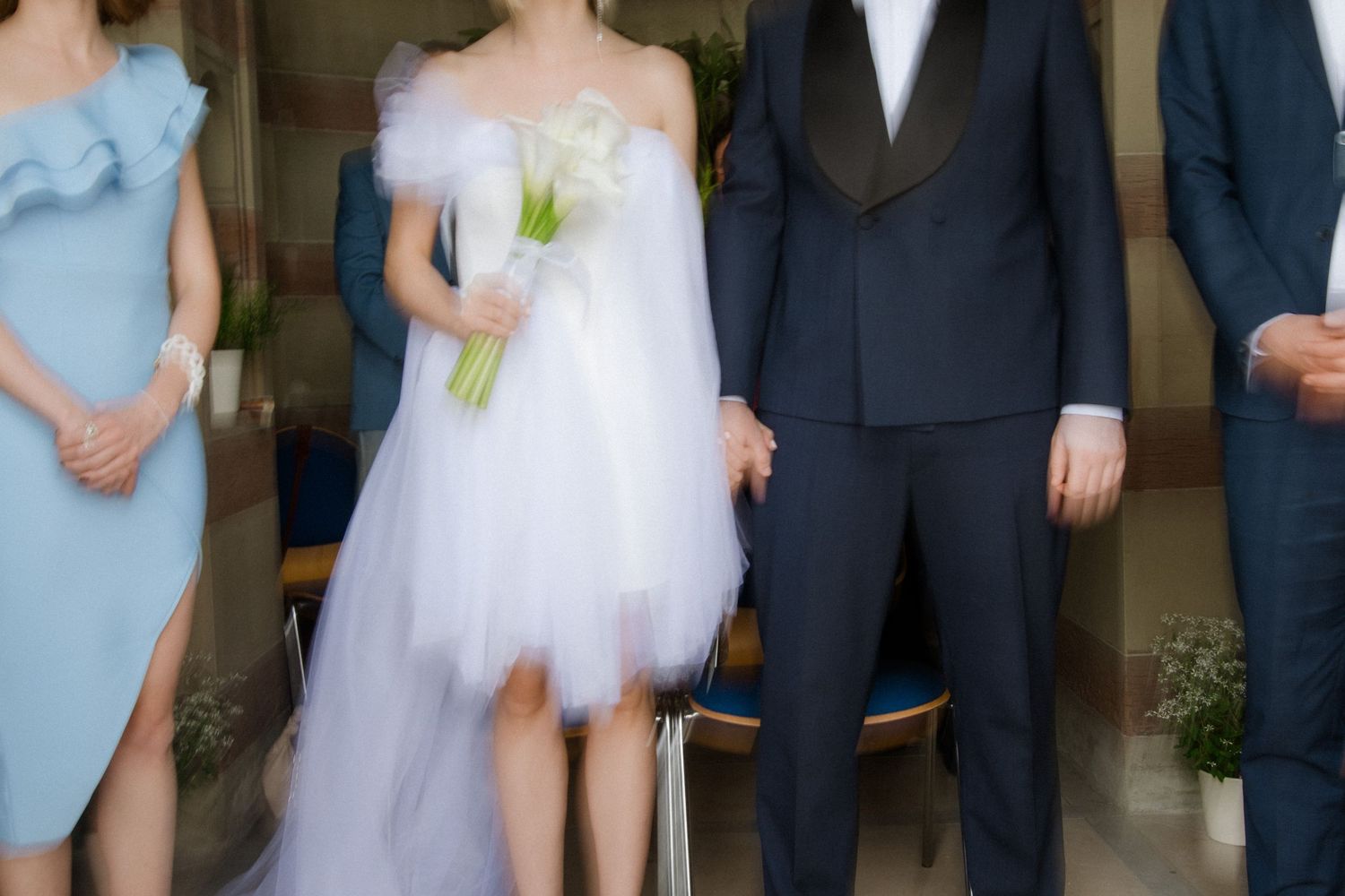 Wedding party with bride in short dress and bridesmaids in blue dresses under architectural details.