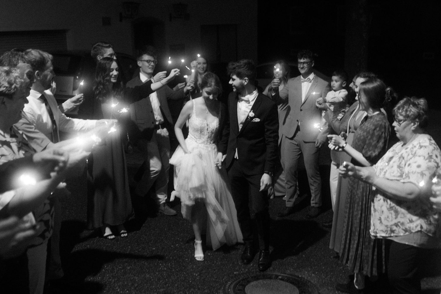 A dimly lit wedding reception scene with guests holding sparklers.