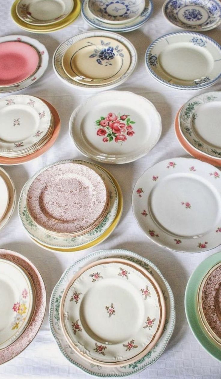 Vintage china plates with floral patterns and delicate designs arranged on a white tablecloth.