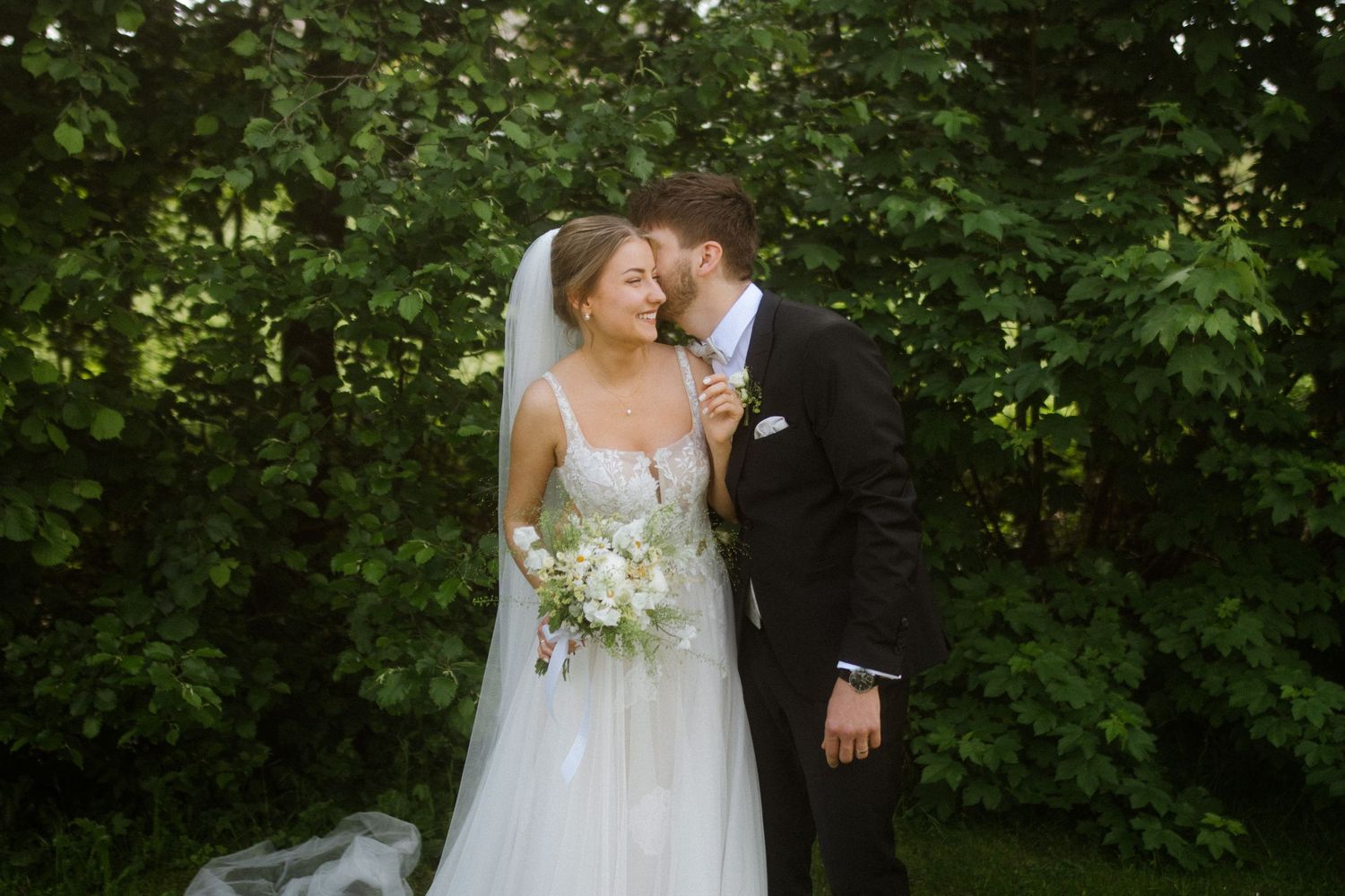 Wedding couple shares an intimate moment in a lush garden setting with the bride holding a delicate bouquet.