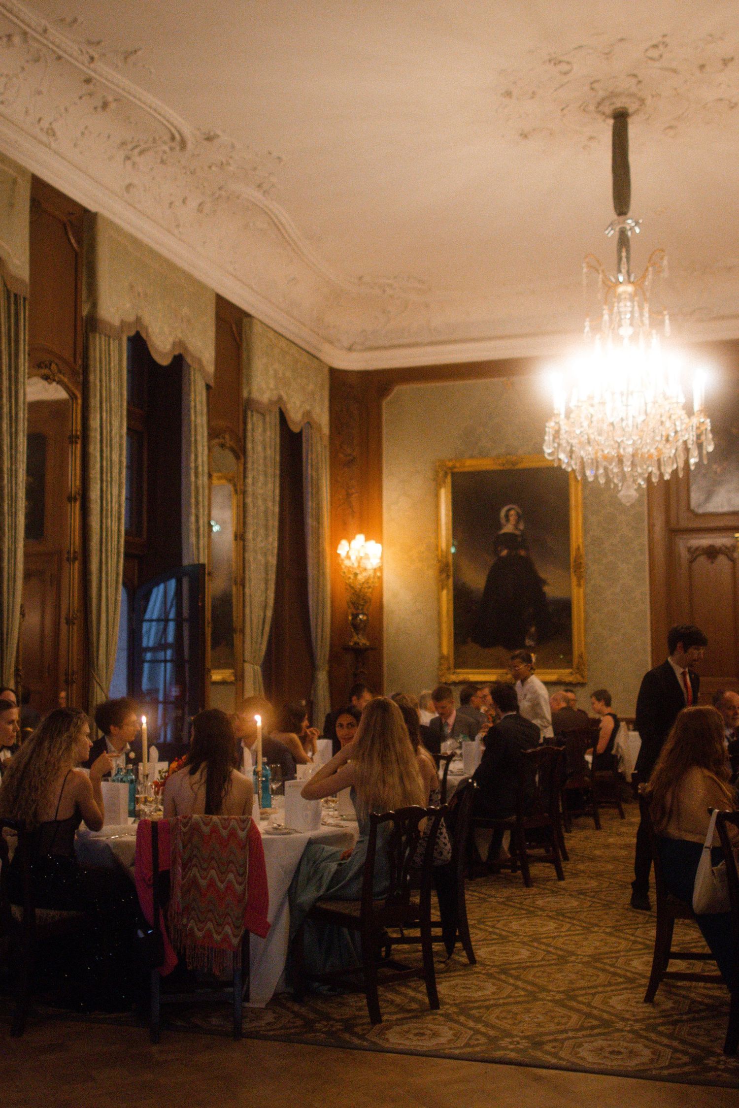 Elegant ballroom with crystal chandeliers and ornate decor illuminated by warm lighting.