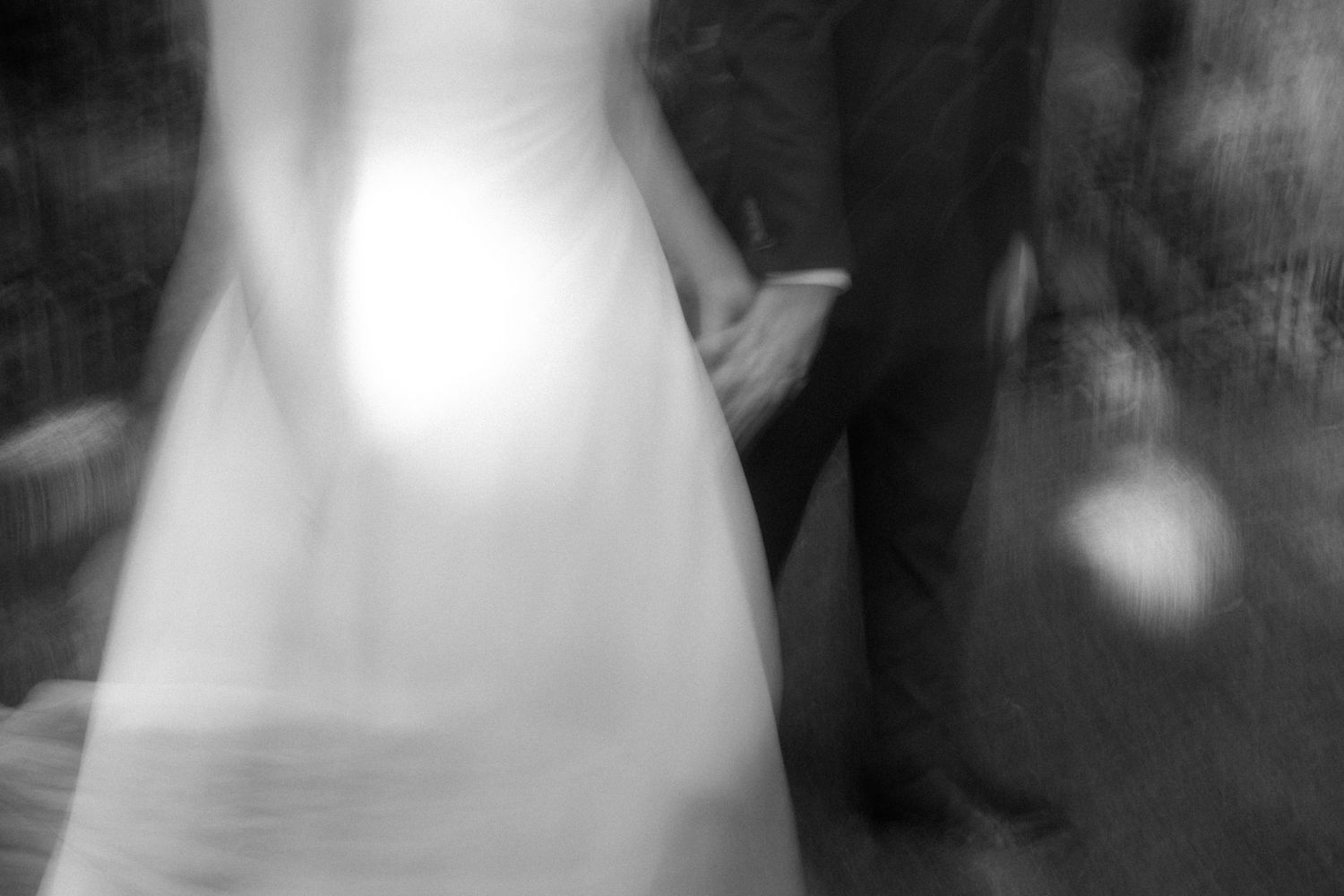 Black and white blurred photo of a bride in white gown holding hands with groom in dark suit at wedding.