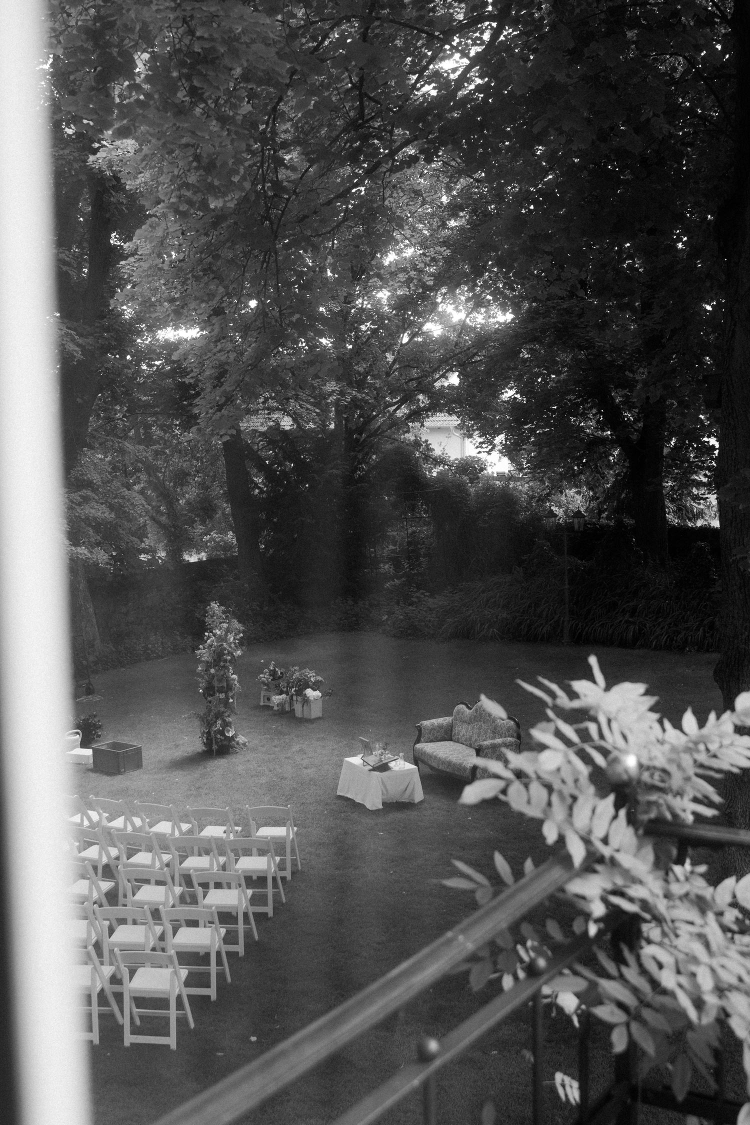Outdoor wedding ceremony setup with white chairs arranged on a lawn under shady trees.