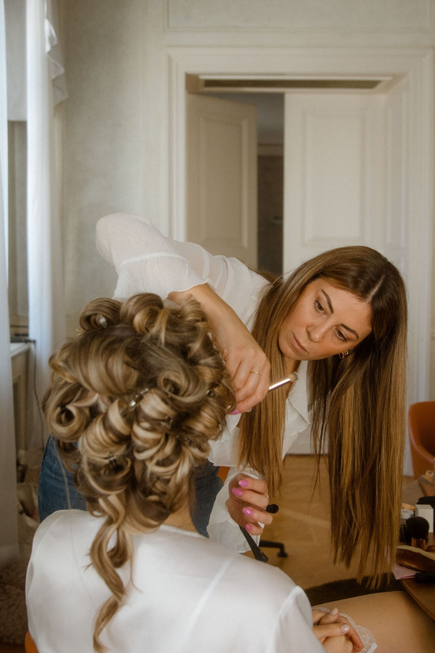 A stylist works on creating an elegant updo hairstyle in a bright room with professional equipment.