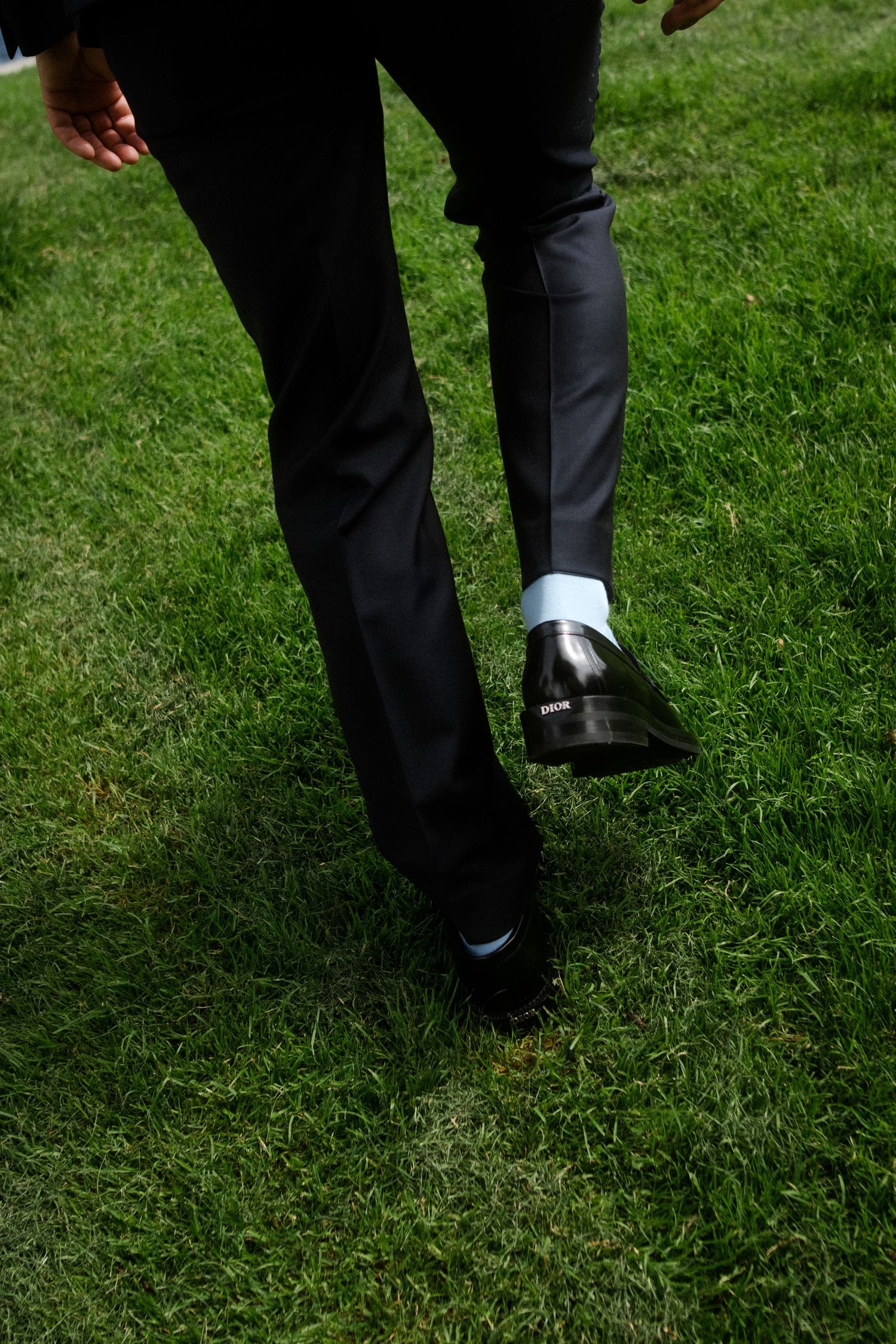 Formal black dress shoes and pants walking on green grass.