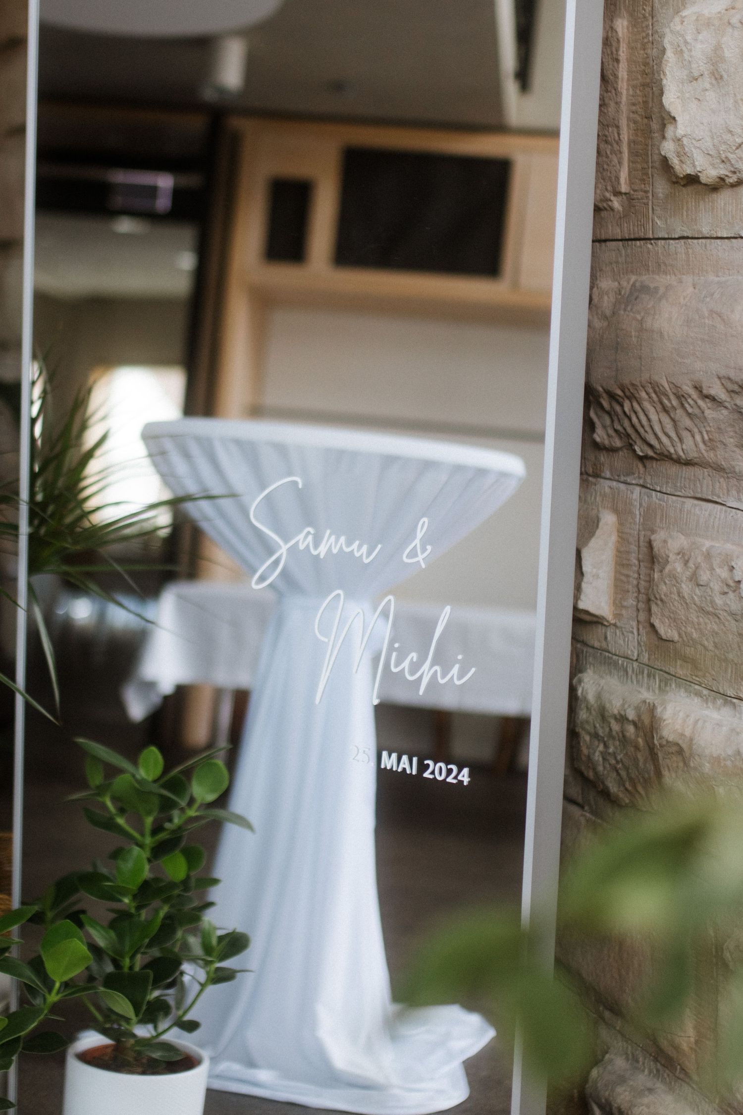 Wedding signage with text overlay reflected in mirror against textured stone wall.