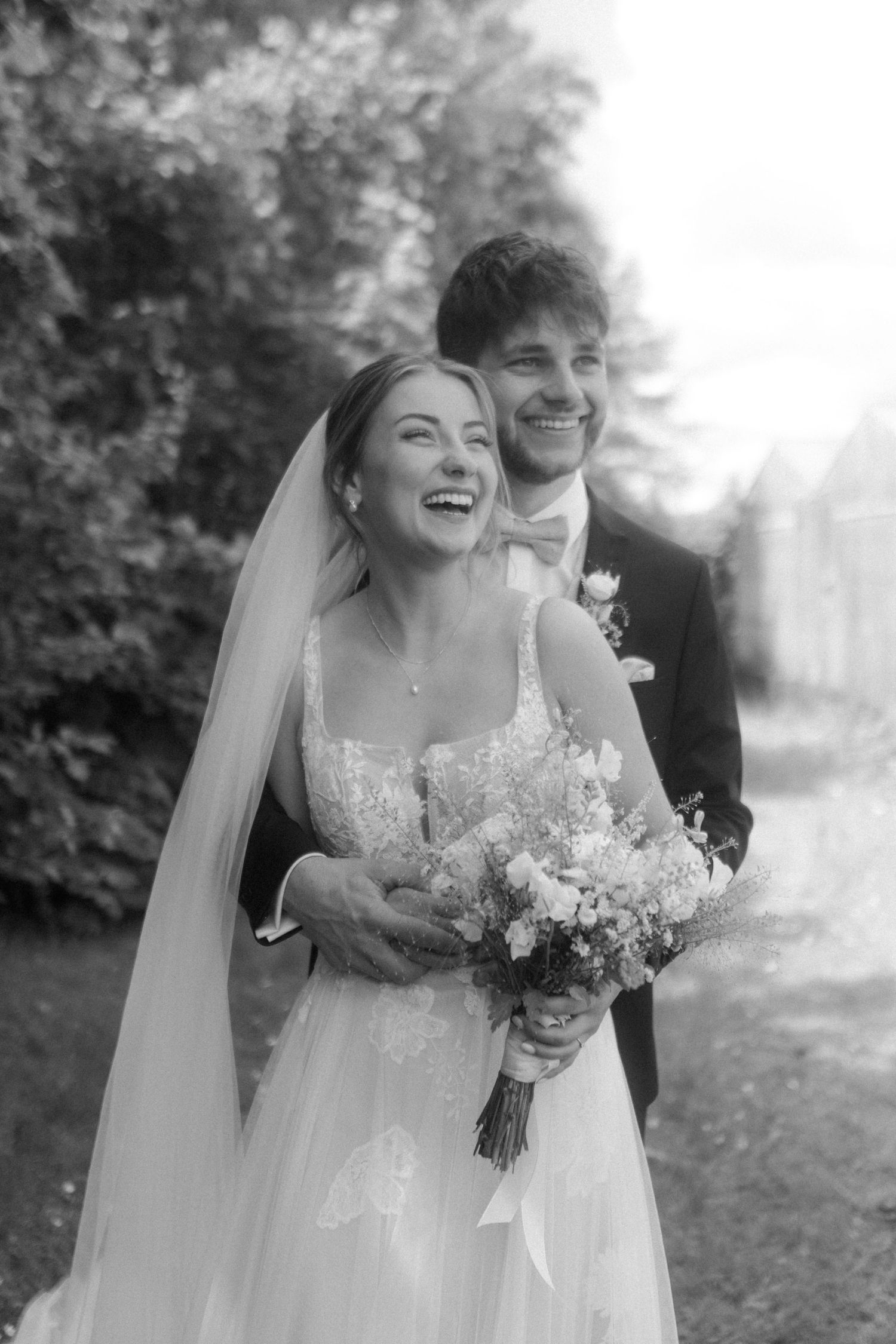 Black and white portrait captures a candid moment of joy and laughter during an outdoor wedding.