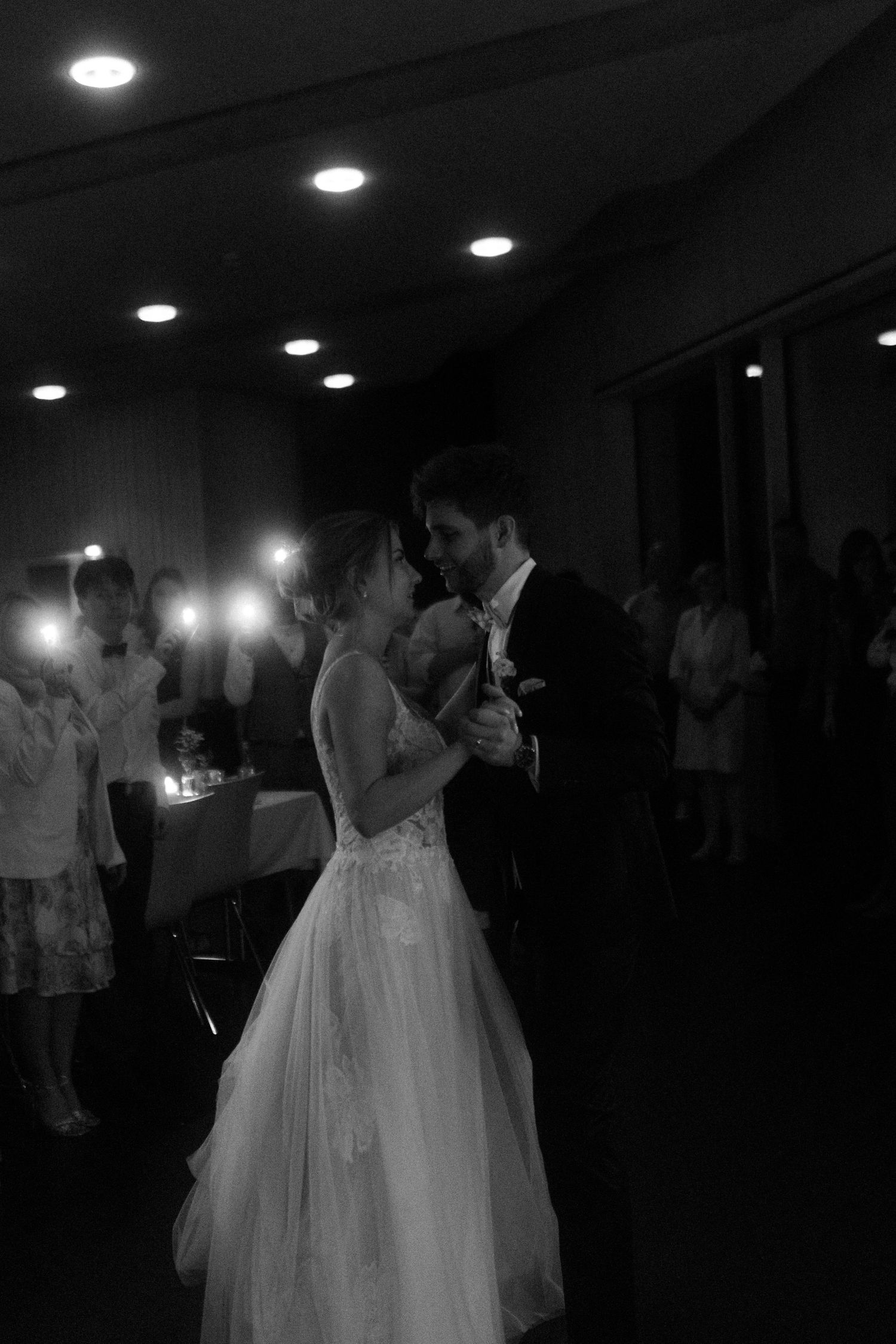A romantic black and white wedding dance scene illuminated by overhead lights.