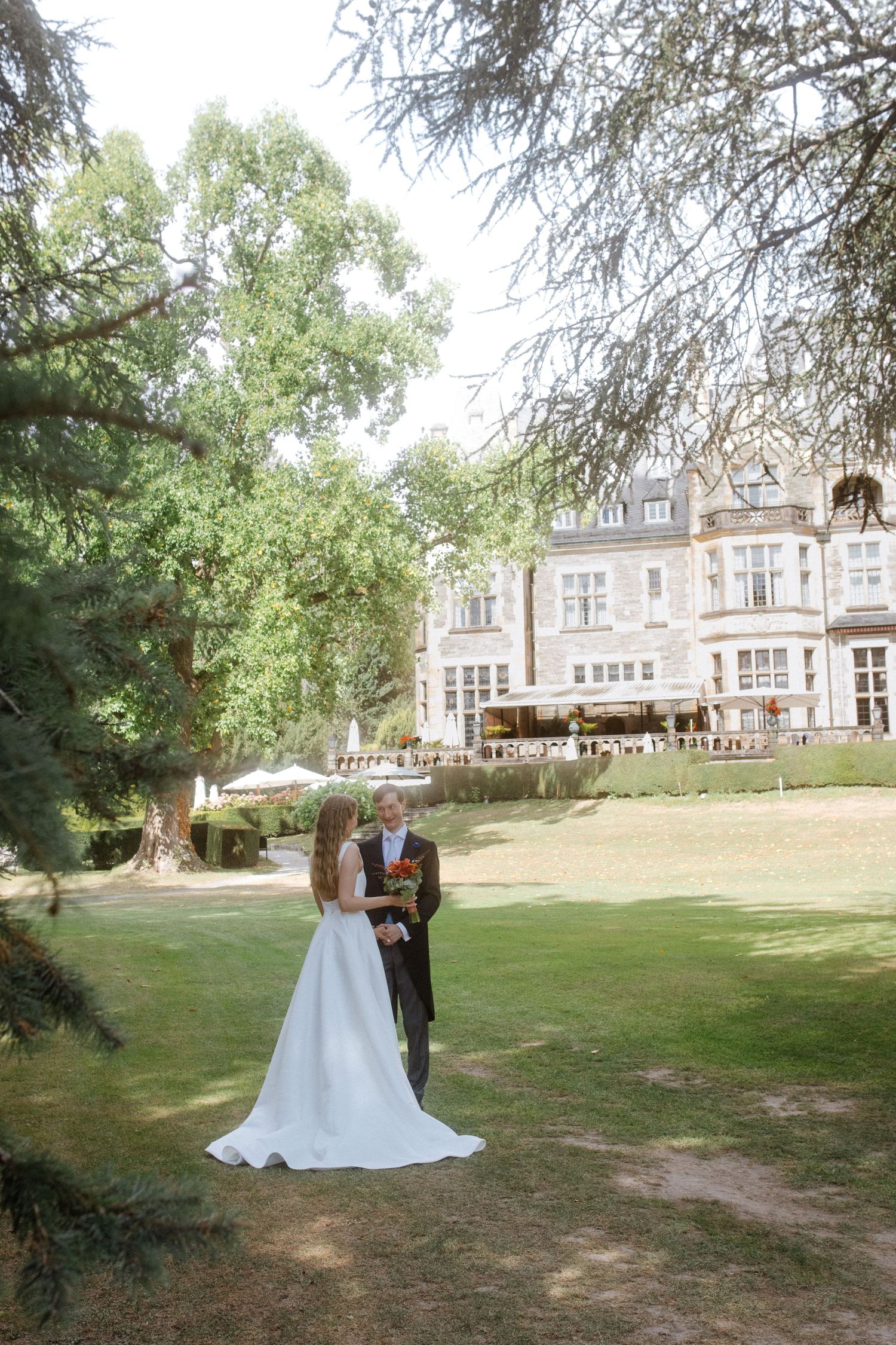 Wedding photography session on sprawling lawn with elegant mansion and mature trees in background.