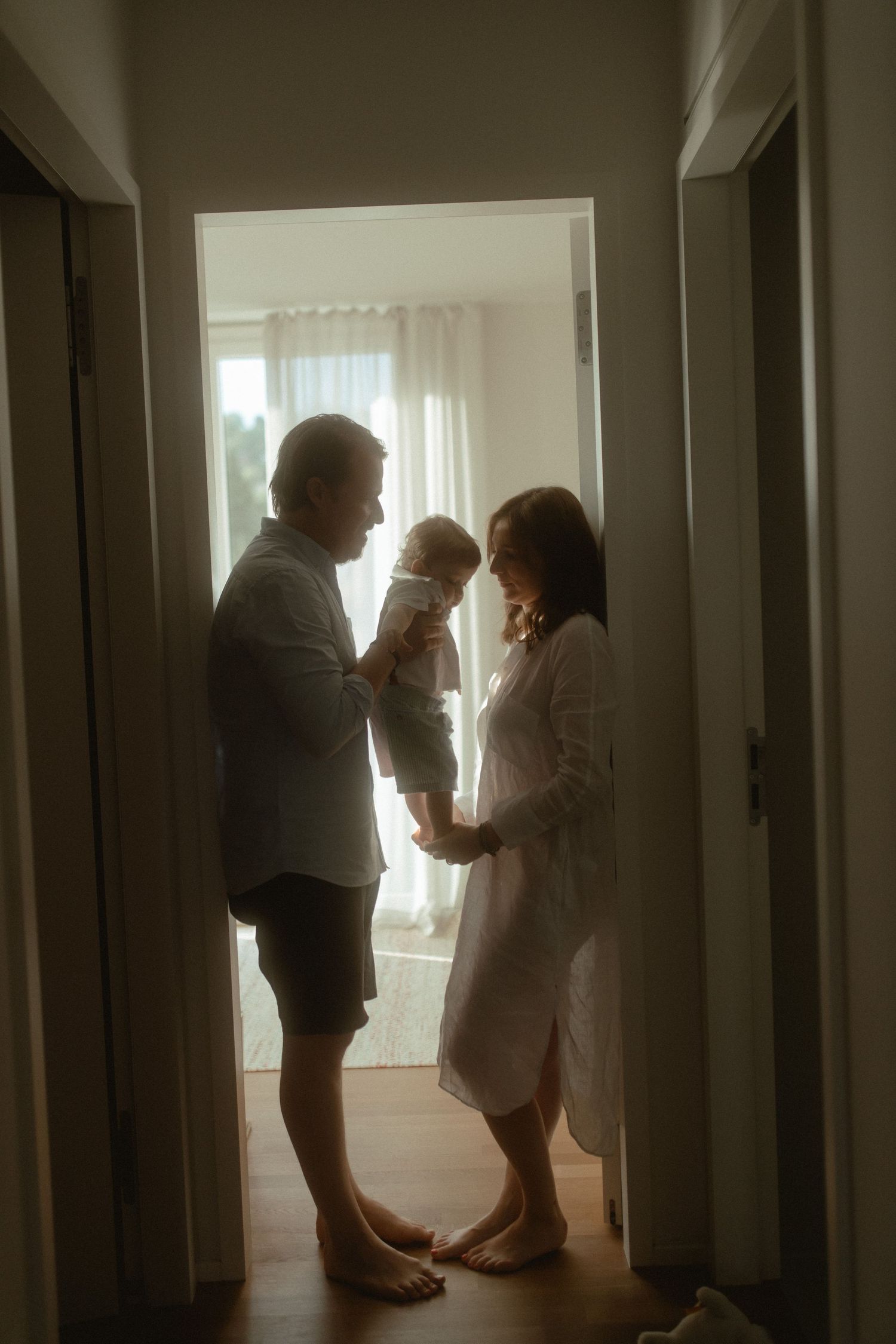 A series of intimate silhouettes showing gentle interactions in a bright, minimalist hallway setting.