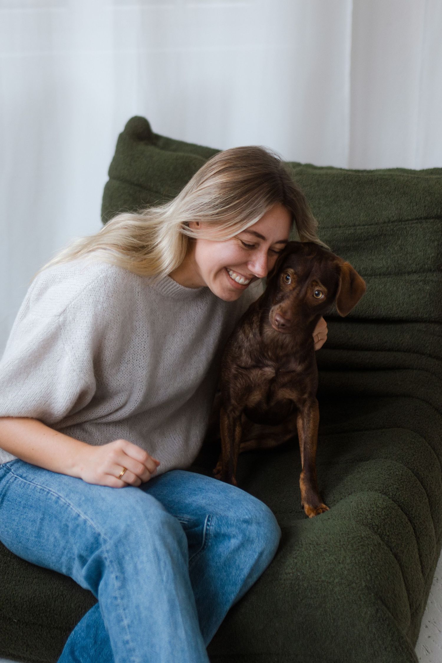 Joyful interaction between a person and a chocolate lab on a dark green couch.