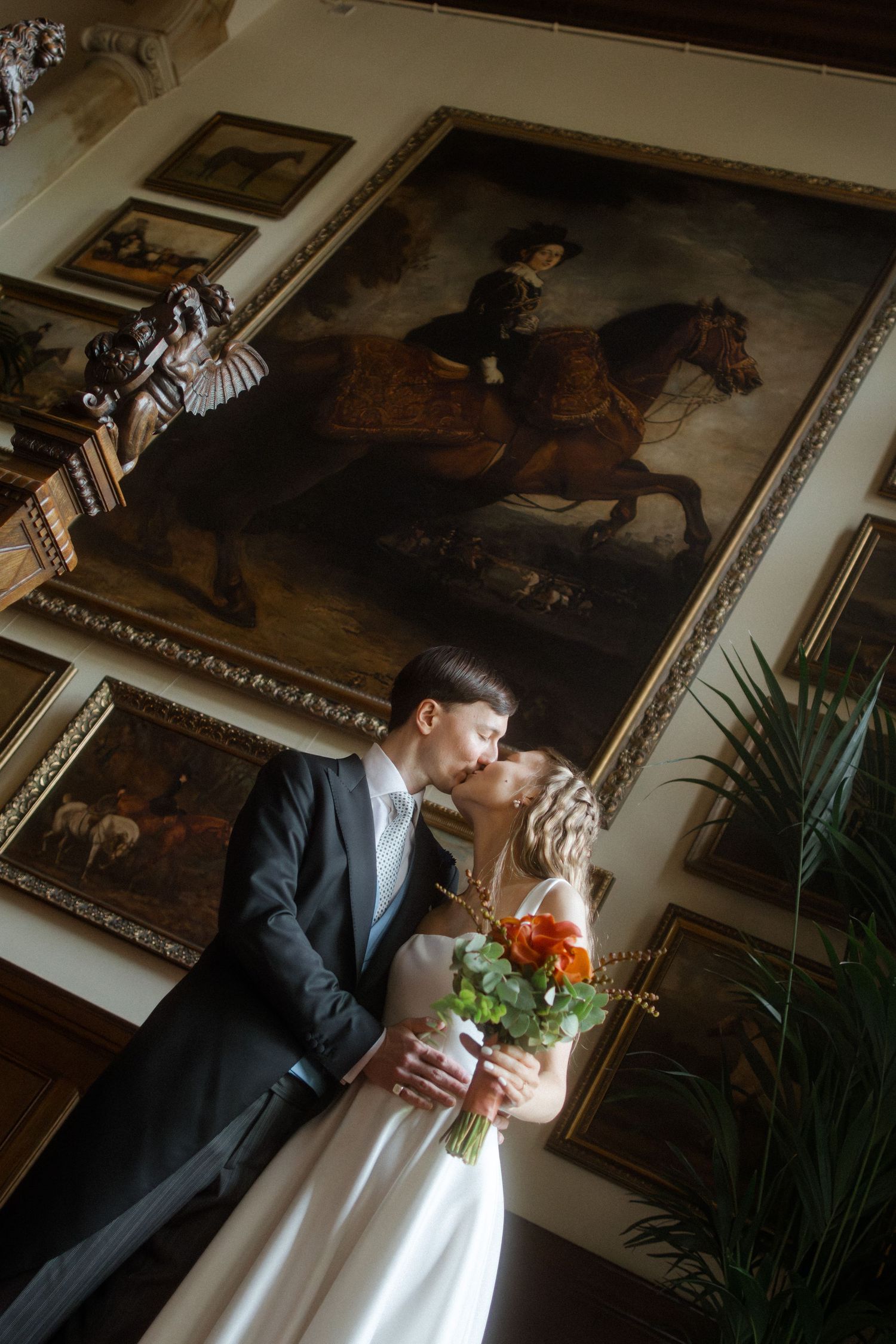 Wedding couple posing in front of classical paintings in an ornate gallery setting.