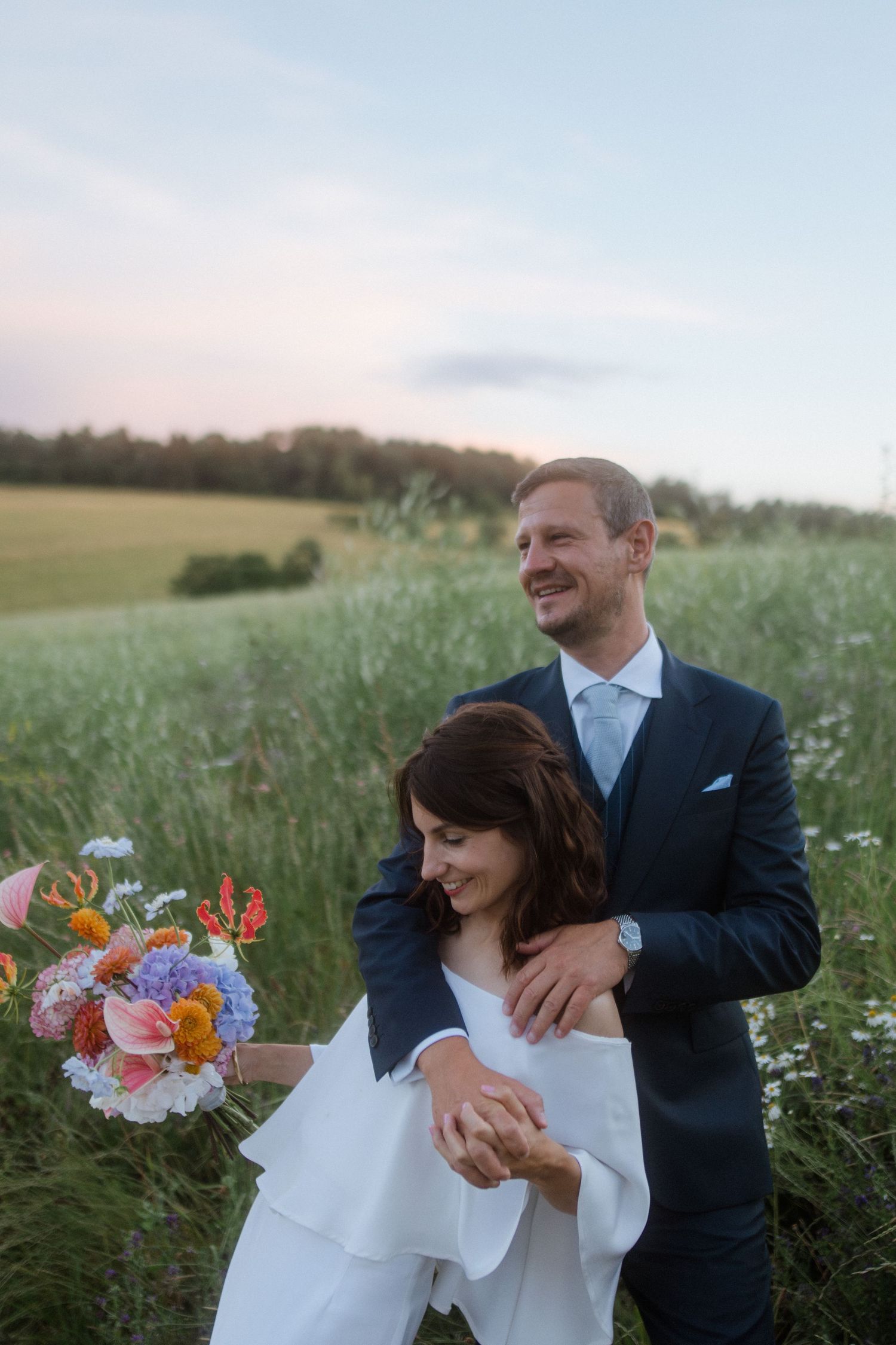 Romantic wedding couple embracing in a wildflower meadow at sunset.