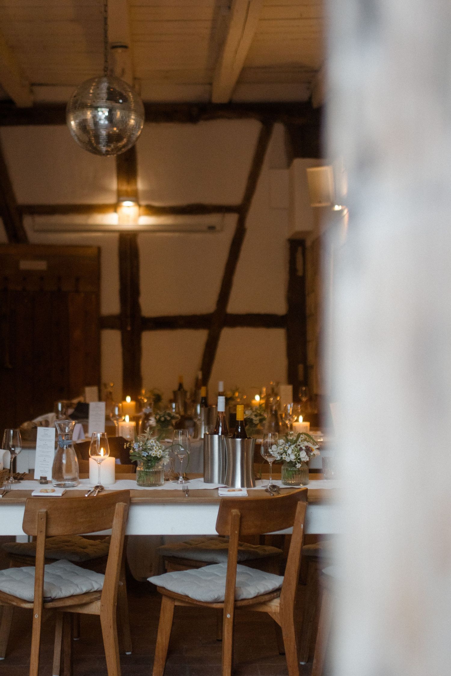 Elegant wedding reception tables set with candles and white linens in a rustic indoor venue.