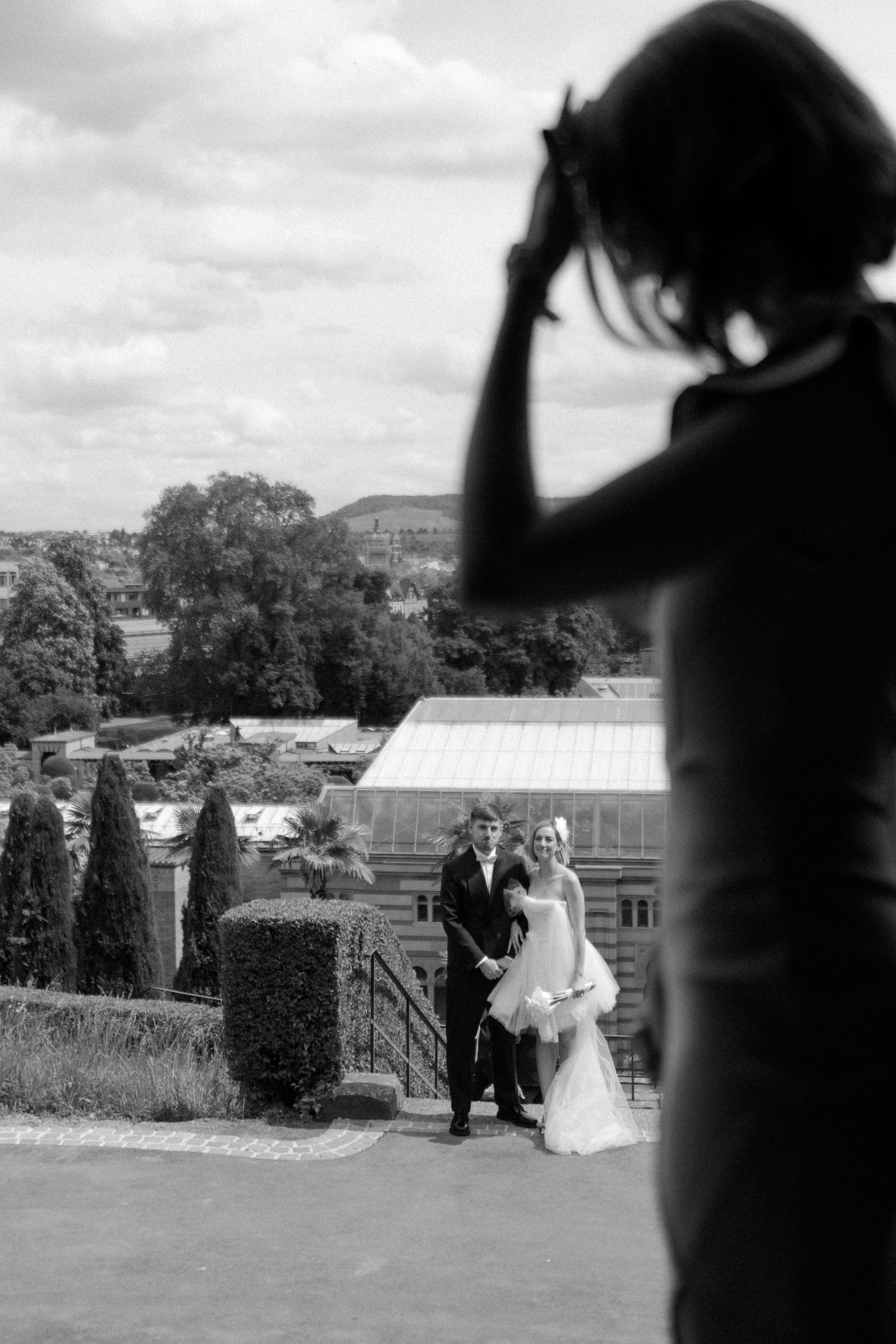 A black and white photo showing a couple posing near garden steps with a greenhouse in the background.