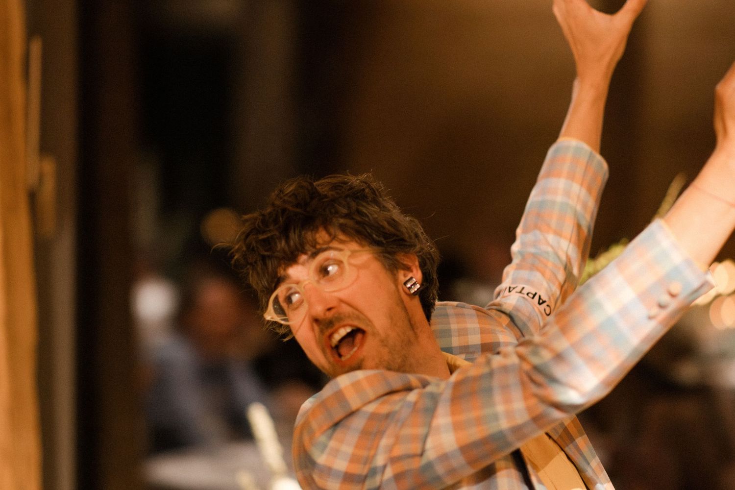Excited young man with curly hair raising arms in celebration at a lively indoor event or party.