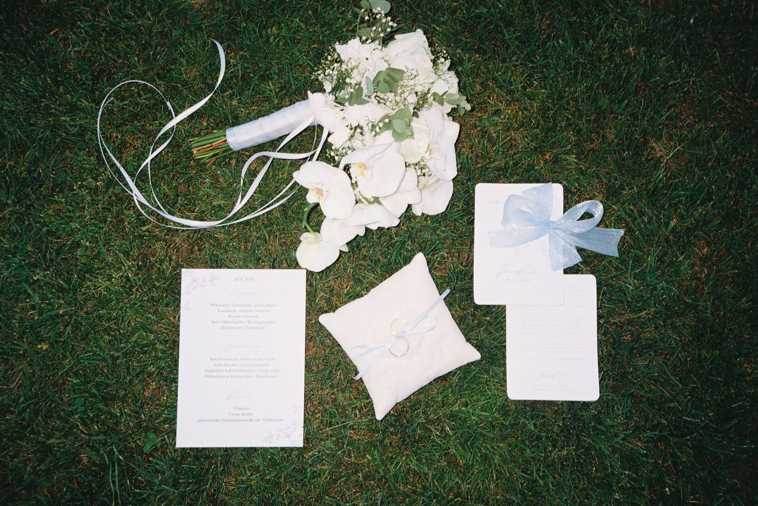 Wedding invitation cards and envelopes scattered on green grass in an artistic arrangement.