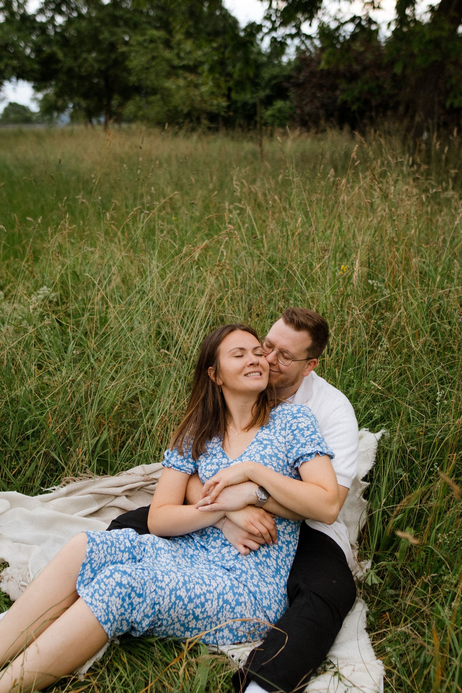 Two people share an intimate moment while lying on a blanket in a grassy field.