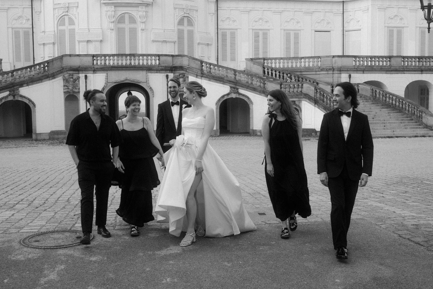 Wedding group creates dynamic poses in front of classical European architecture.
