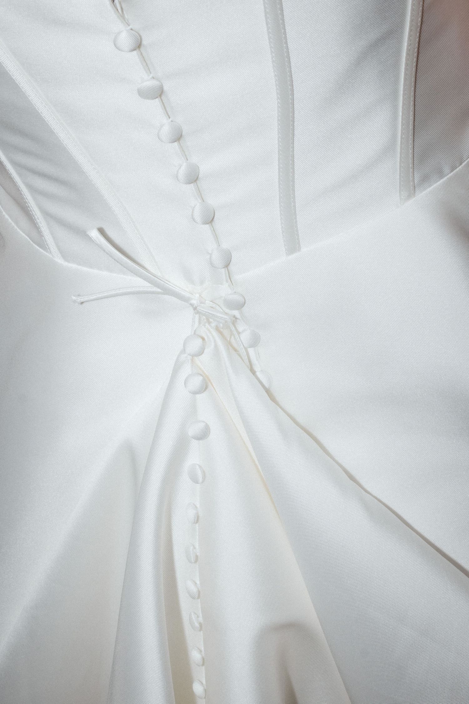 Close-up details of a white wedding dress with delicate fabric and pleating patterns.