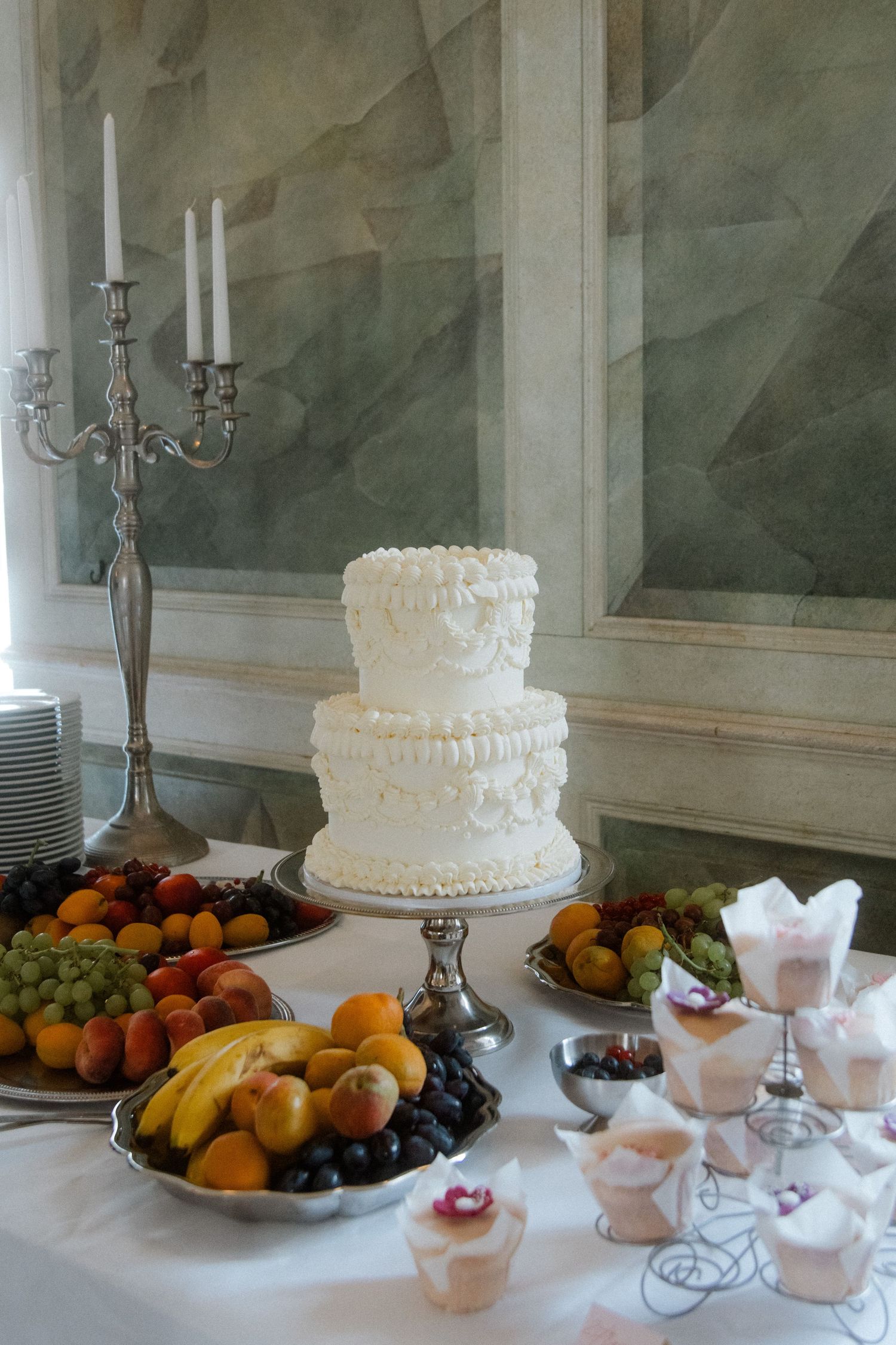 Wedding reception dessert table with white cake, fruit, and silver candelabras.