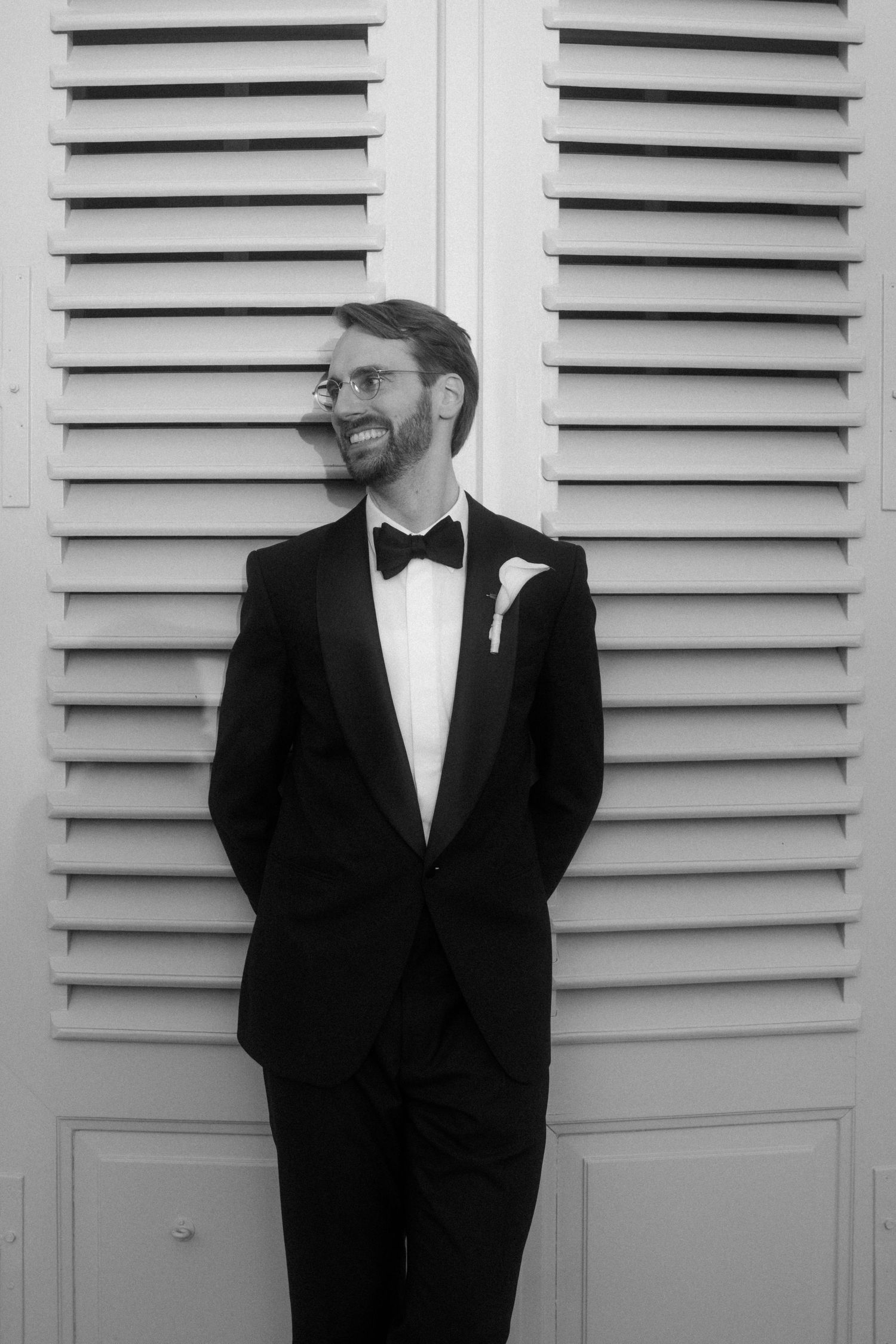 Classic black and white portrait showing details of a tuxedo bow tie and lapel against white shutters.