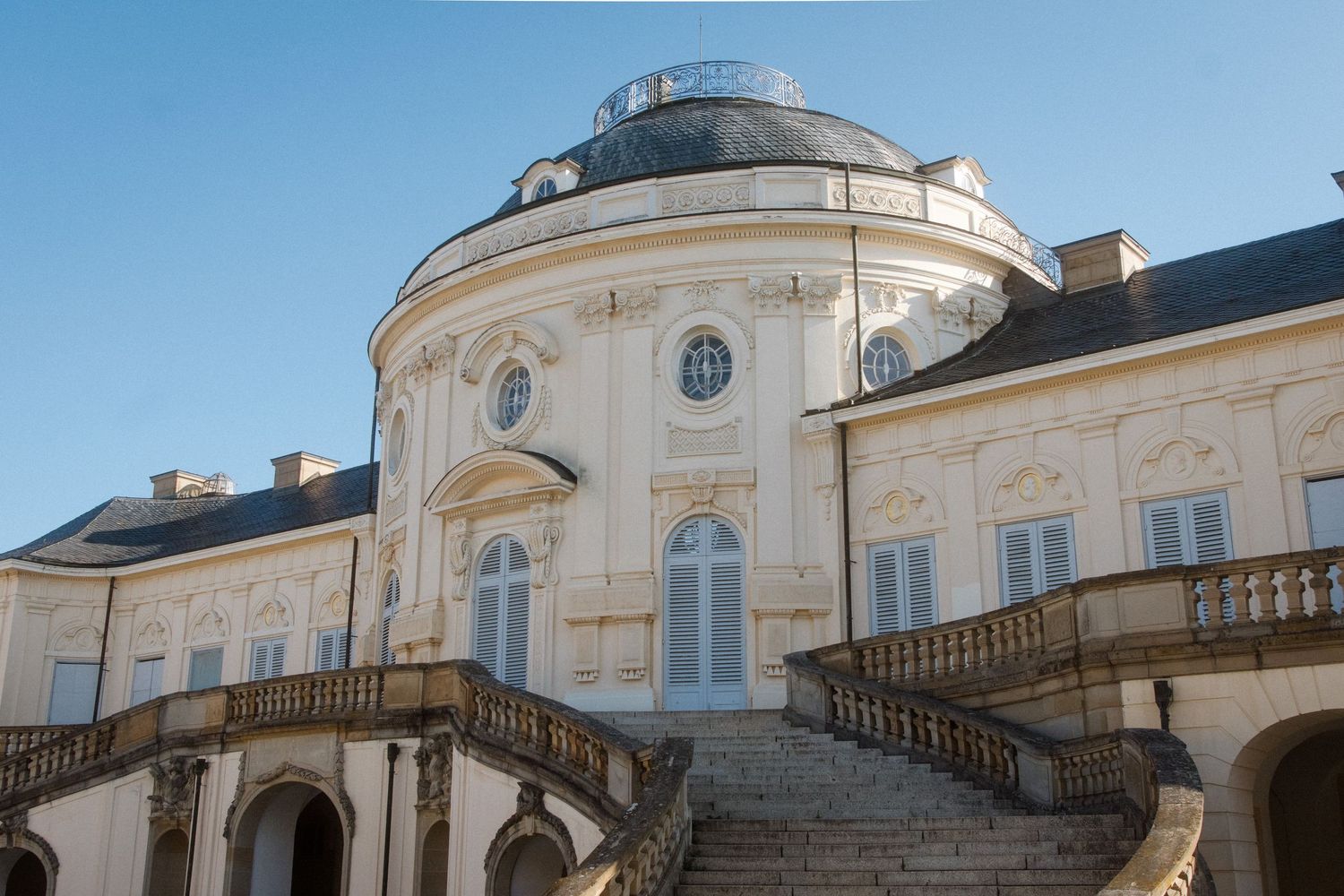 Panoramic view of a grand palace with domed roof and symmetrical staircases.