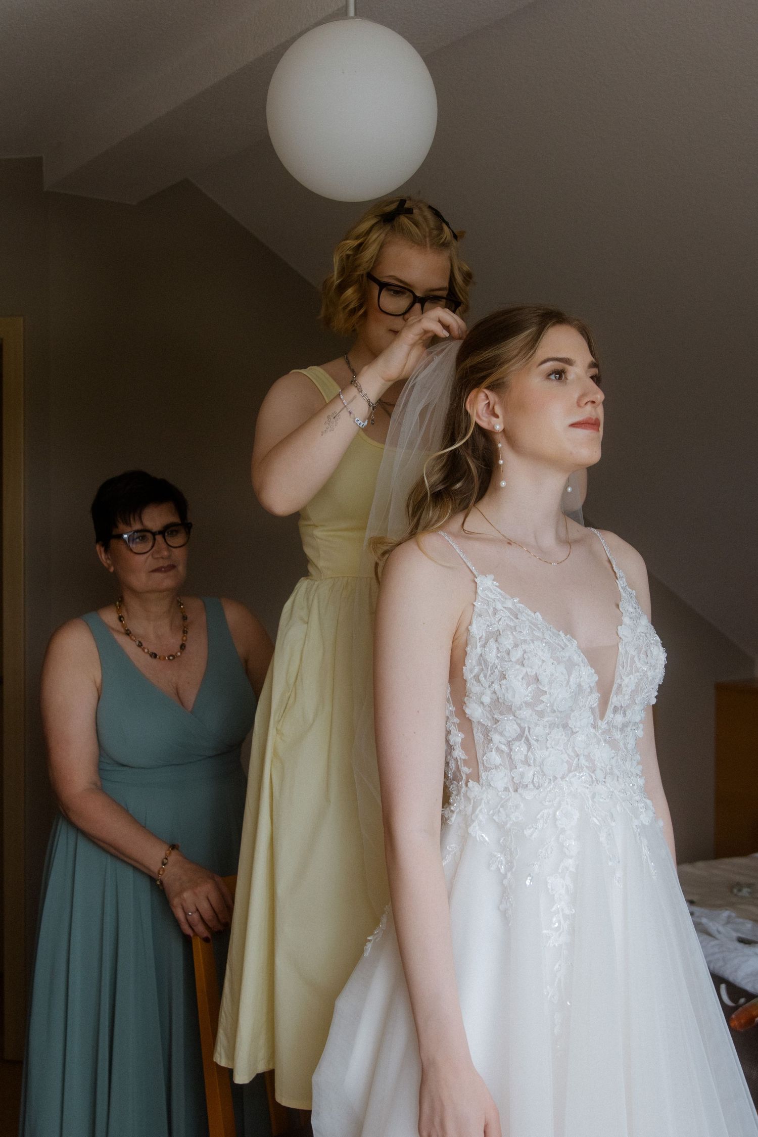 Wedding dress fitting scene with bridesmaids in mint green dresses helping with final adjustments.