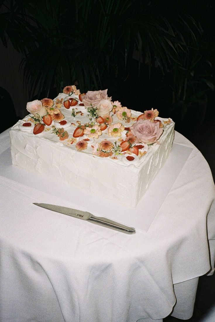 Rectangular white wedding cake decorated with fresh strawberries and flowers on a white tablecloth.