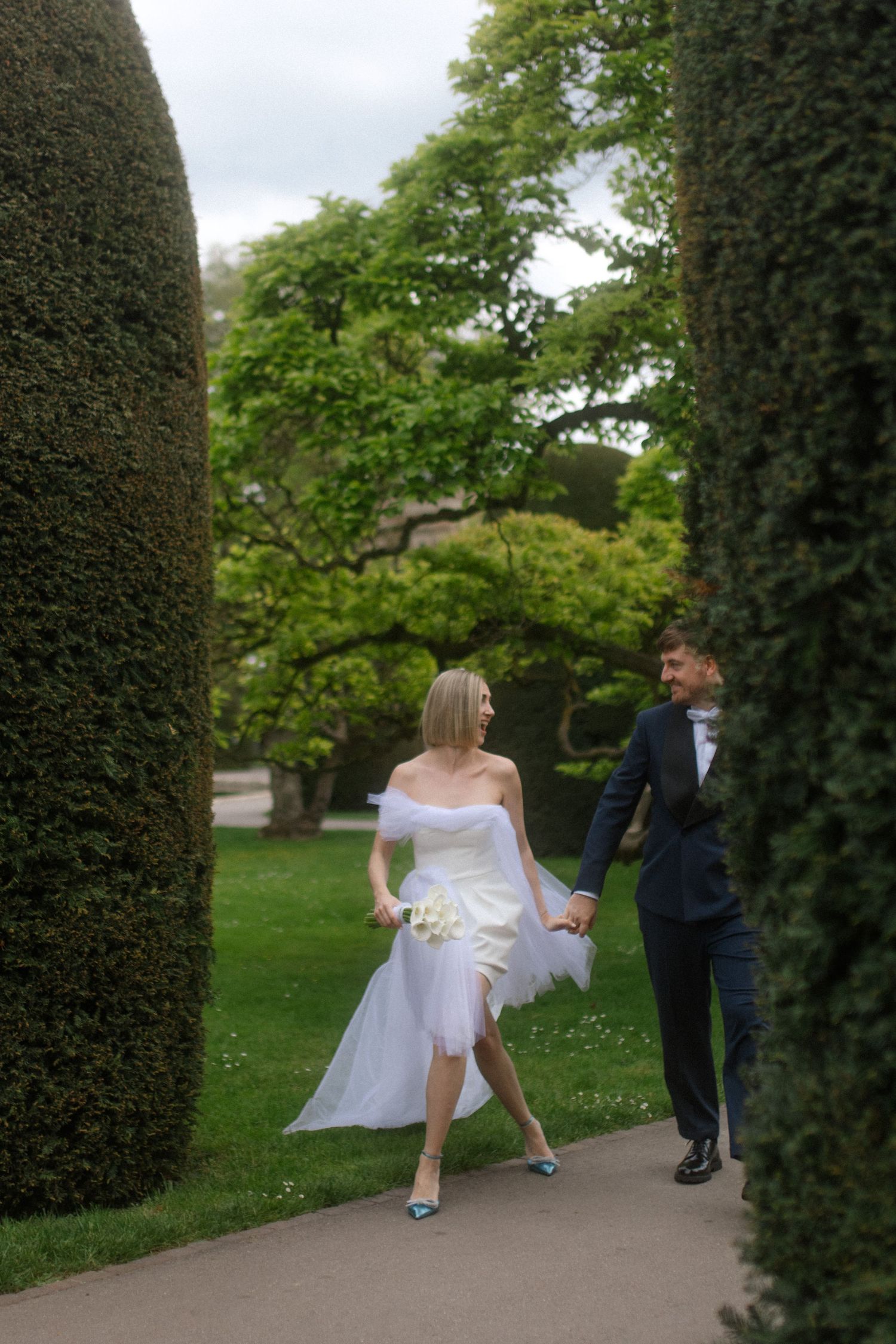 Couple walking through manicured hedges in a formal garden during their wedding photoshoot.