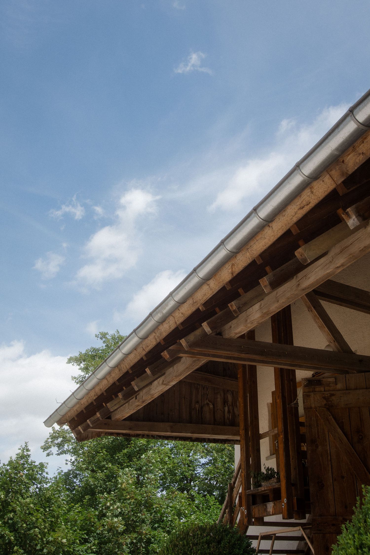 Rustic wooden roof beams and overhanging eaves against bright blue summer sky.