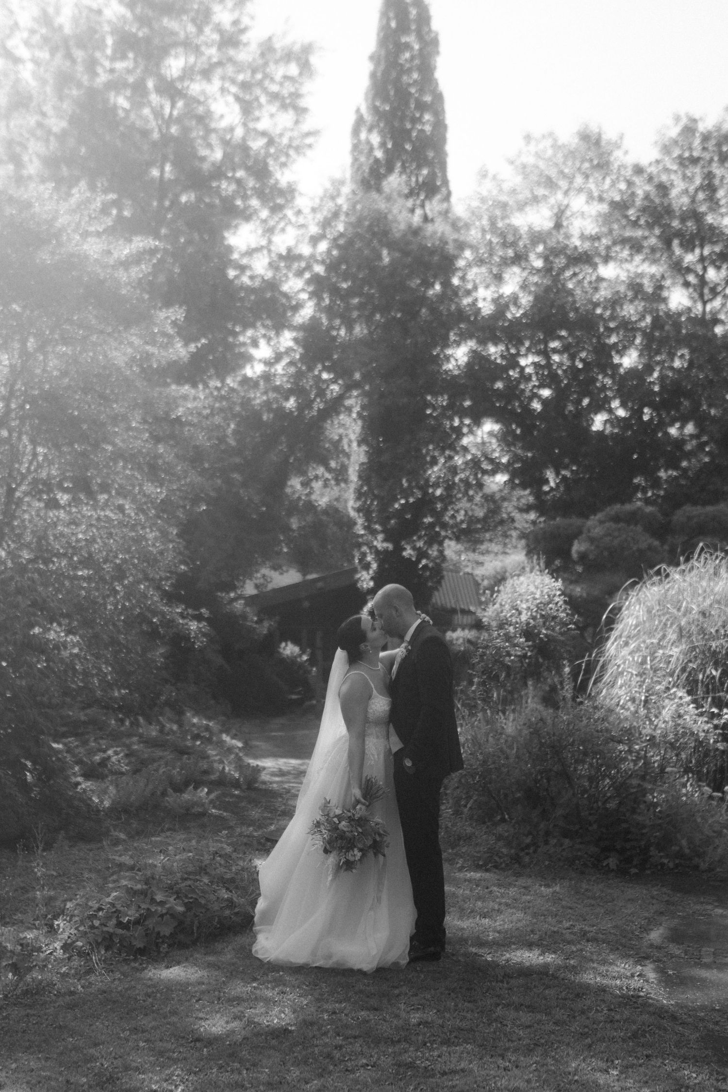 Romantic black and white moment of newlyweds in a sunlit garden setting.