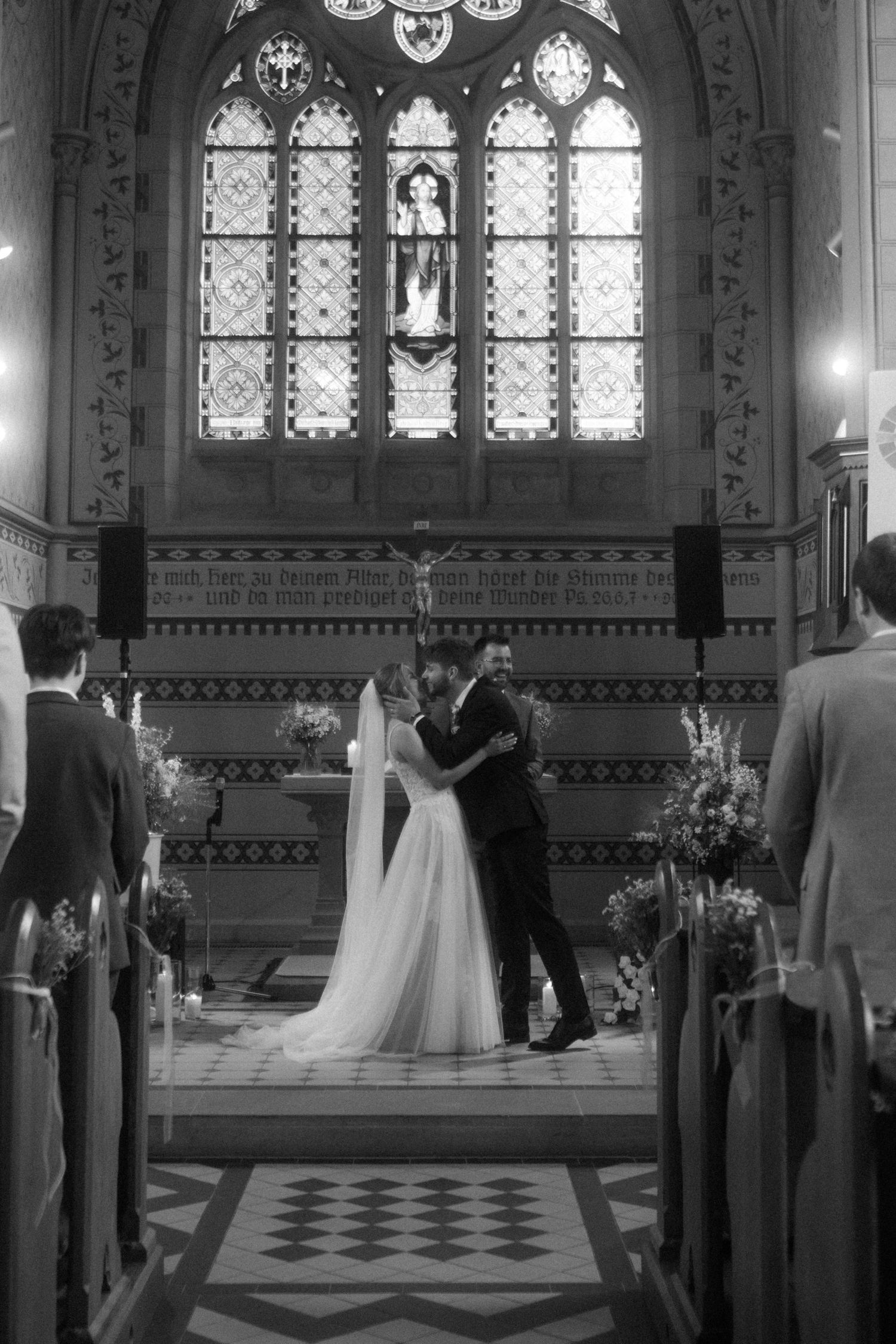 Church wedding ceremony with stained glass windows and couple at altar in black and white.