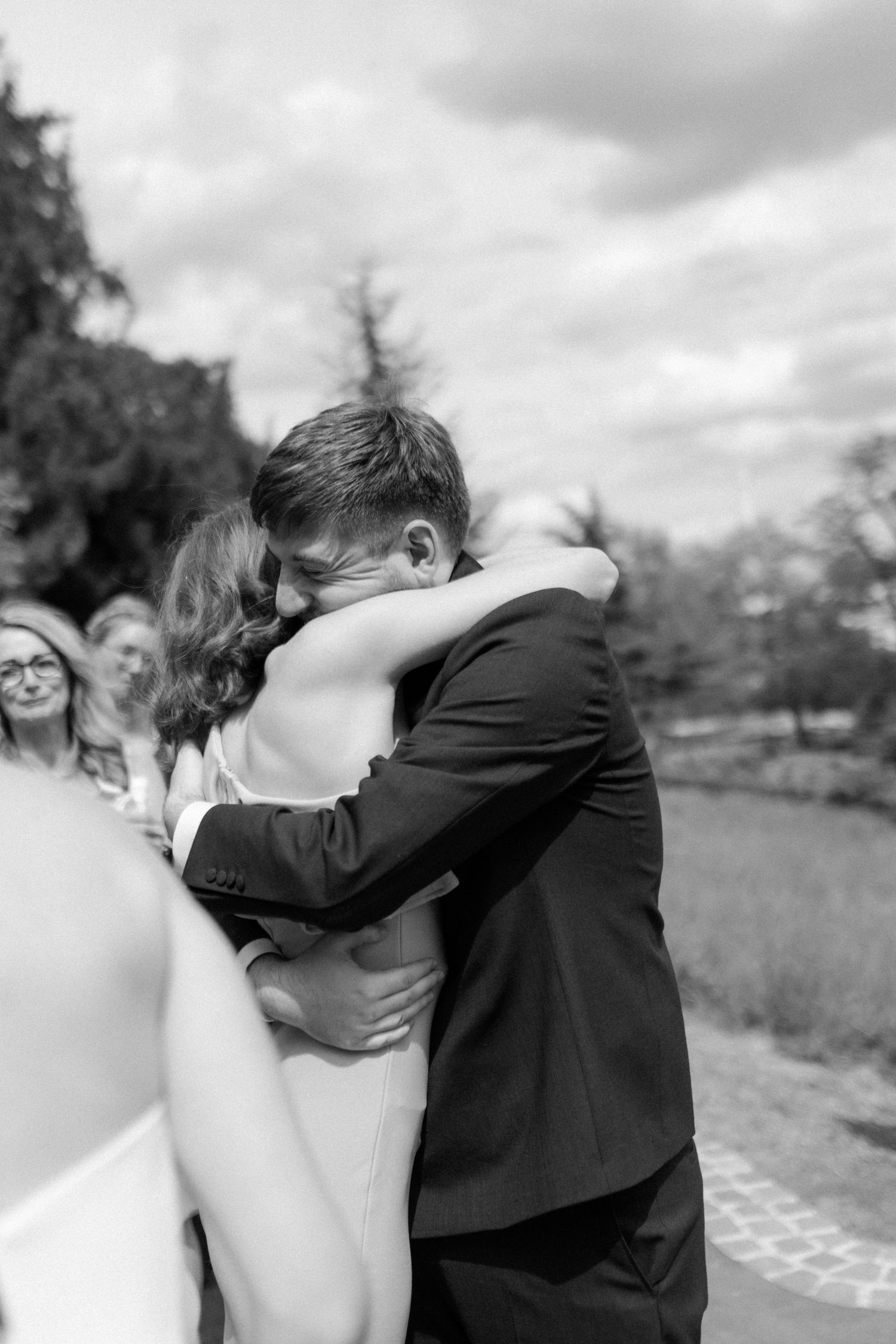 An intimate black and white photo capturing an emotional embrace at an outdoor wedding.
