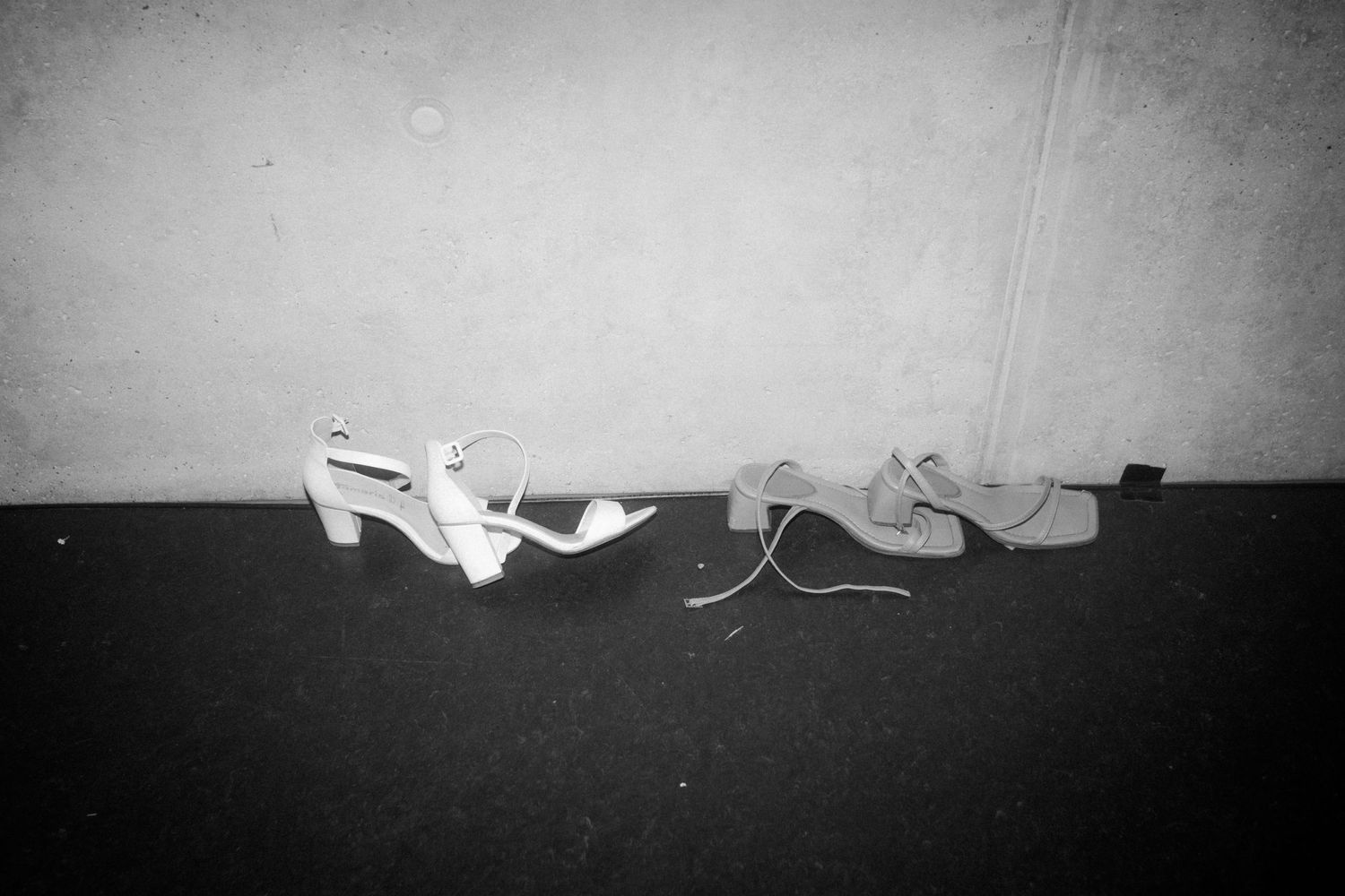 Wedding shoes lined up against a dark wall in black and white.