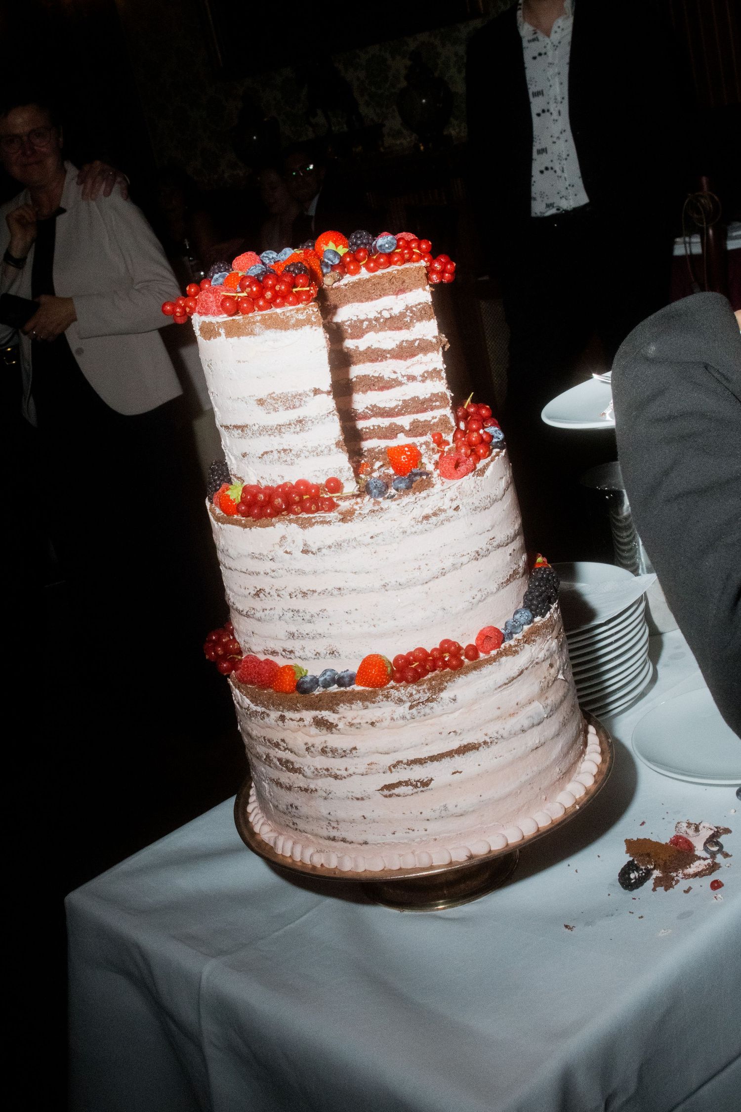 A tiered wedding cake decorated with fresh red berries sits on a white tablecloth.