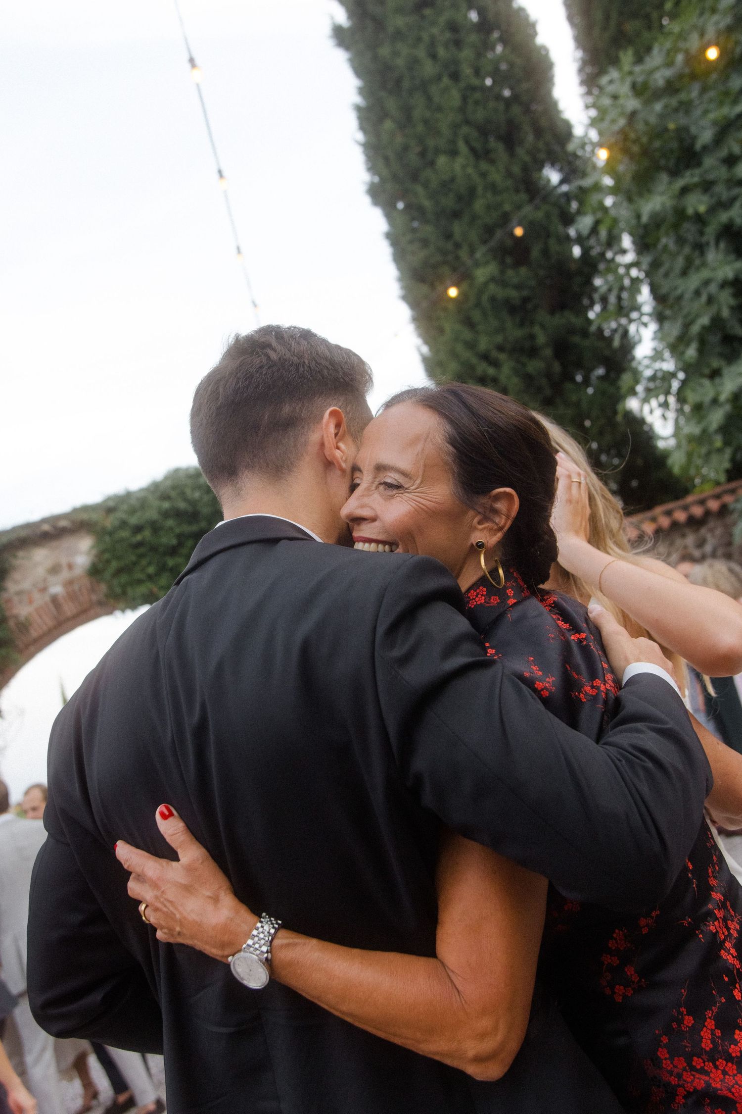 Wedding guests embrace during emotional dance moment at outdoor reception.