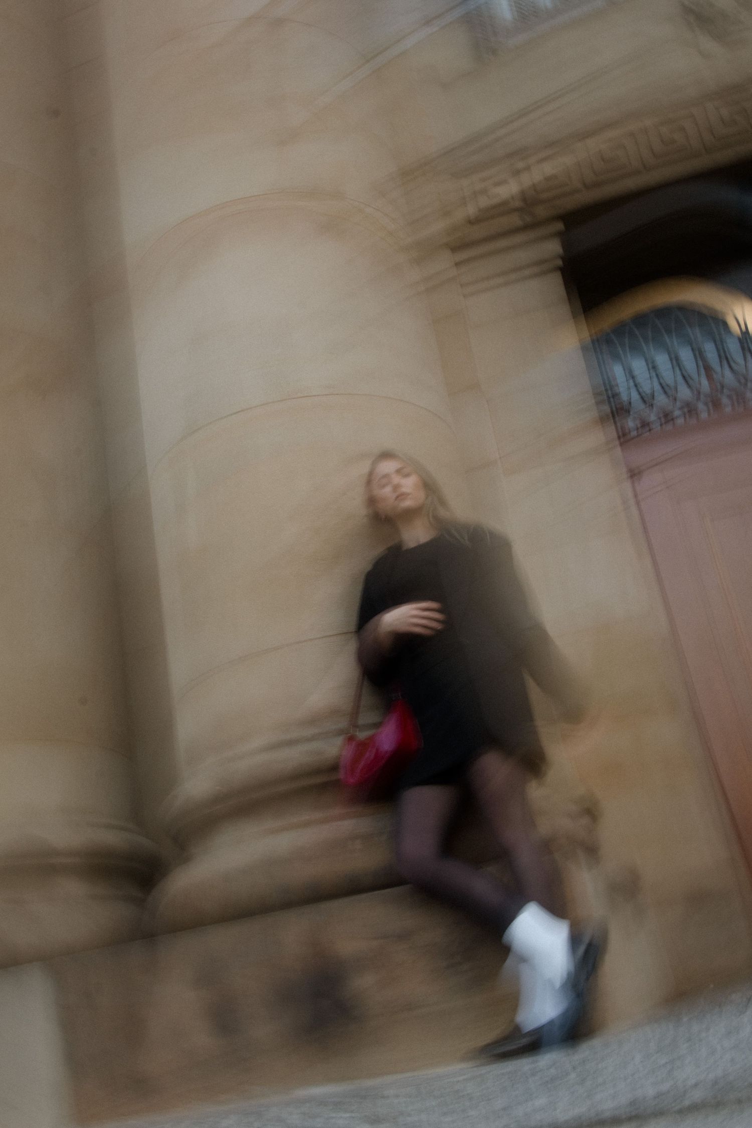 Motion blur sequence of a person walking past stone columns in an urban setting.