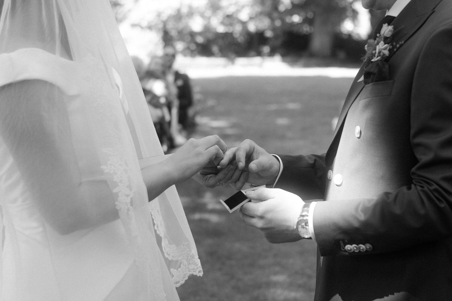 Close-up of wedding ring exchange during outdoor ceremony.