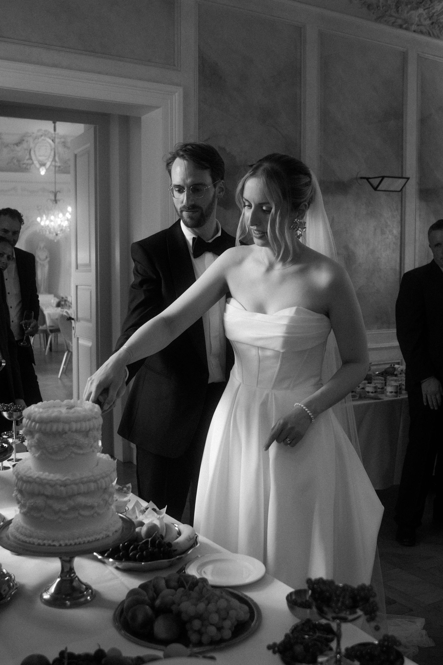 Wedding couple cutting their white tiered cake at an indoor reception.