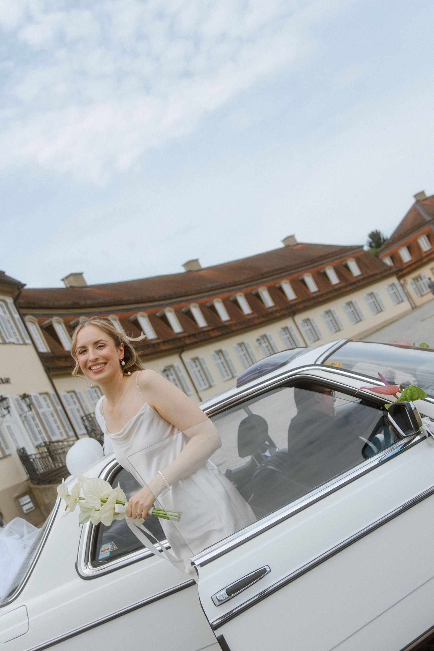 White vintage car with passengers in front of a grand historic building.