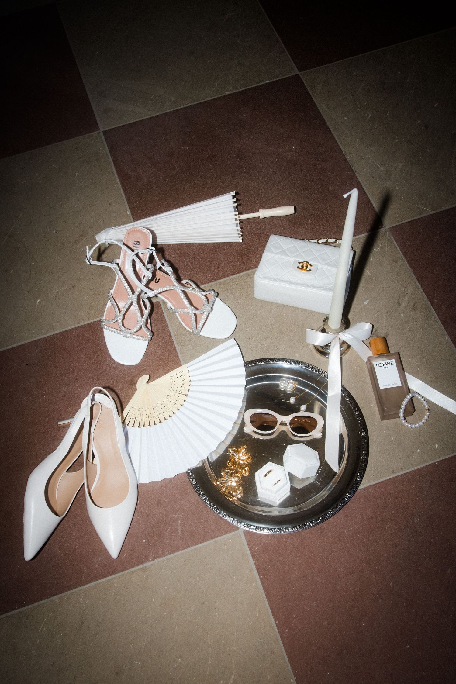 Wedding accessories including white shoes, fan, and decorative items on checkered floor.
