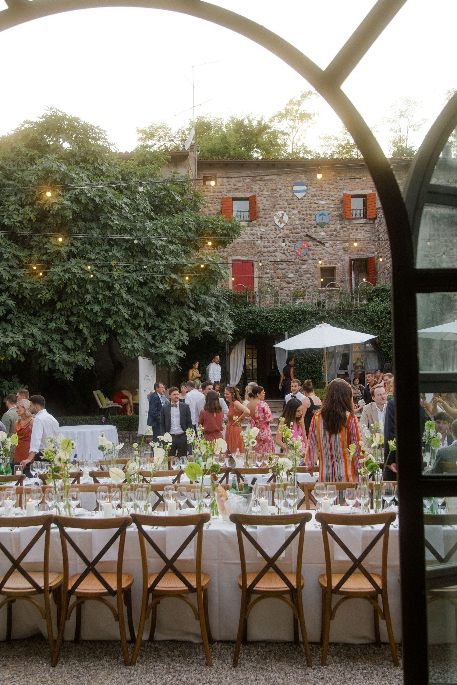 Long rustic dining tables set for an outdoor wedding reception with wooden cross-back chairs.