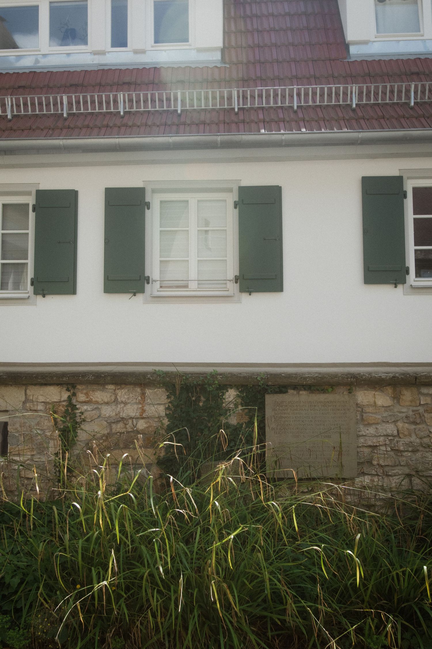 White stone house facade with green shutters and ornate brickwork detail.